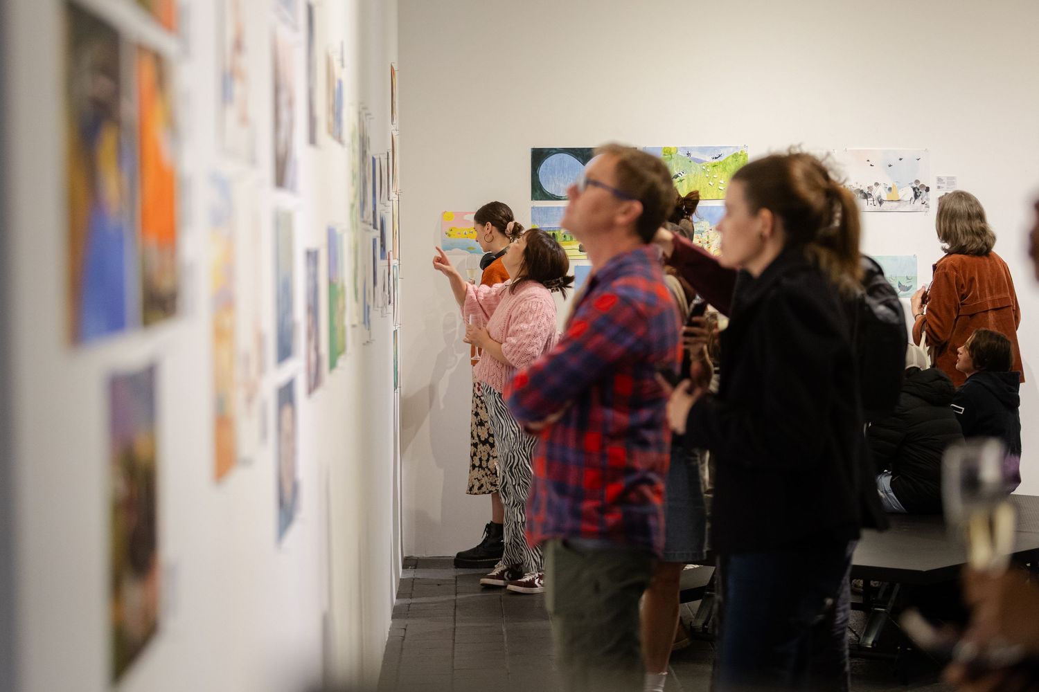 People viewing colorful artwork displayed on white gallery walls during an art exhibition opening event.