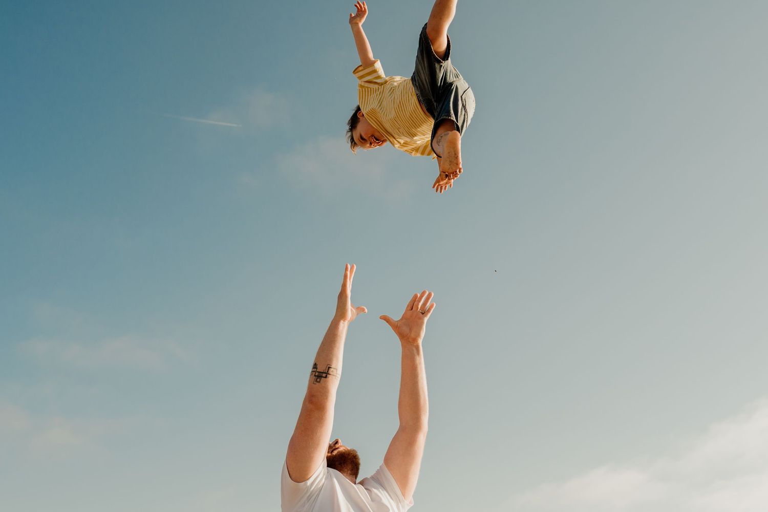 Adult tossing a child high into the blue sky at Godrevy beach during family photoshoot