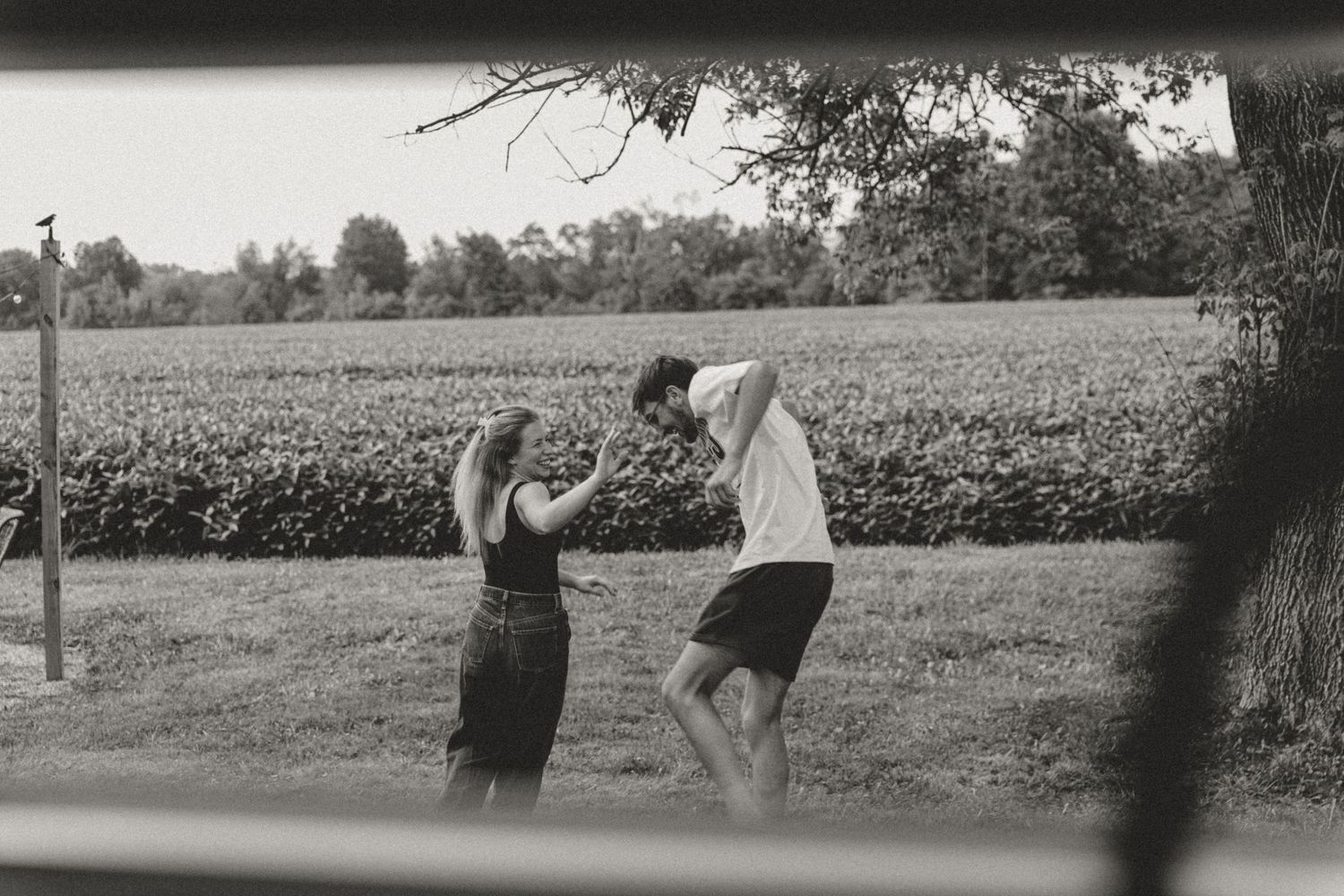 Black and white photo of a couple dancing outdoors near a lush green field on a farm.