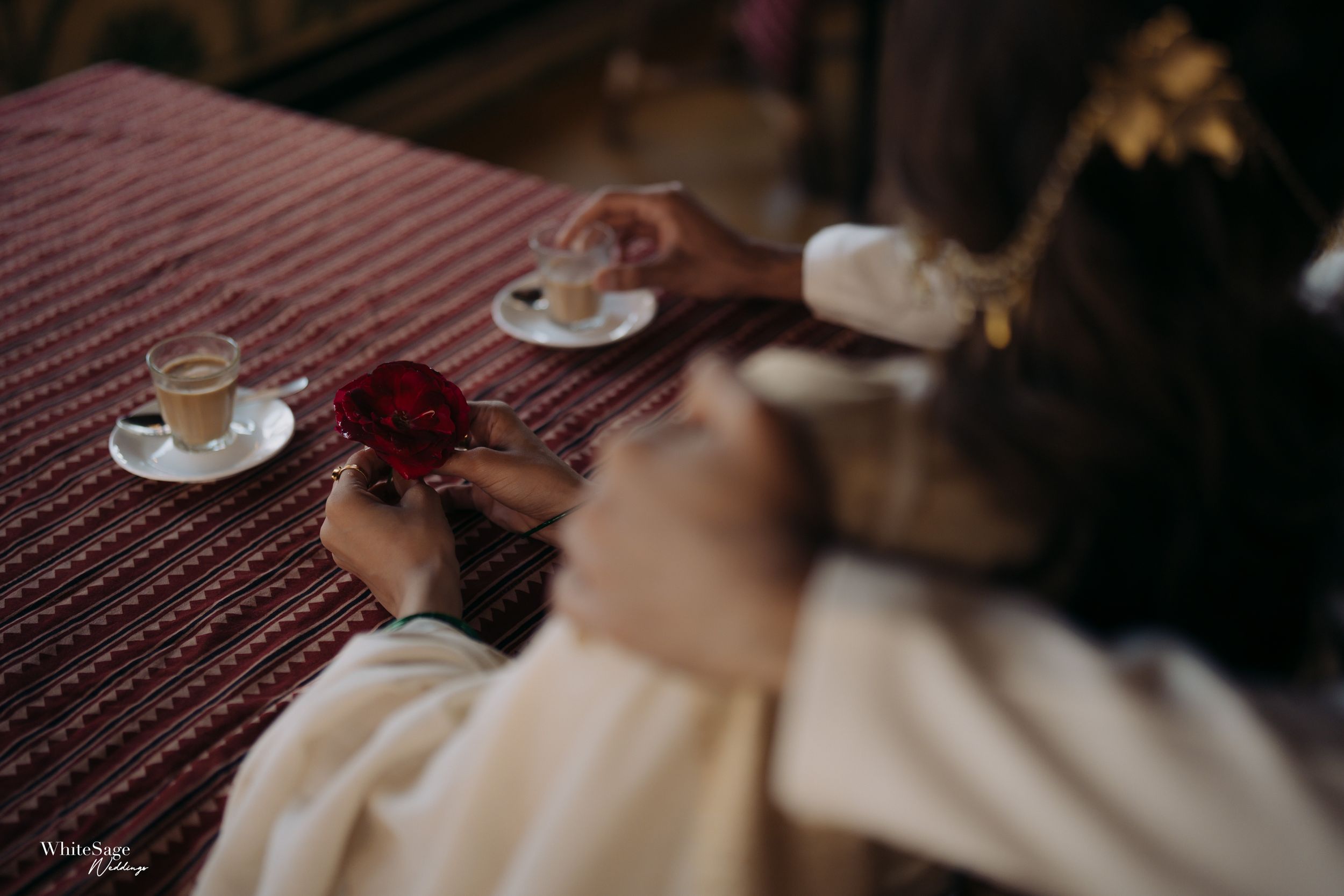 Coffee cups on a striped tablecloth with red roses in a romantic setting.