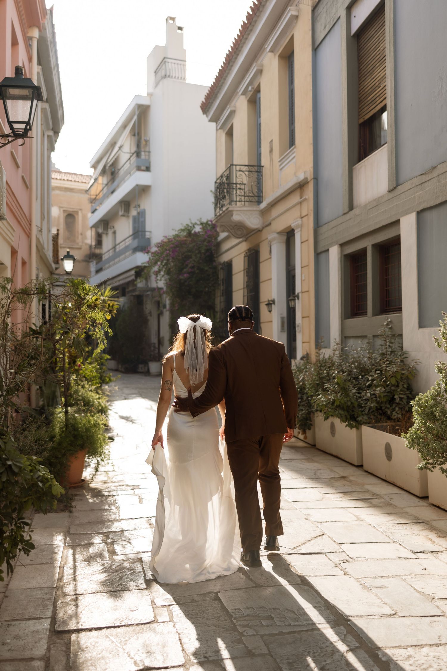 Newlyweds walking down charming European street in afternoon sunlight.