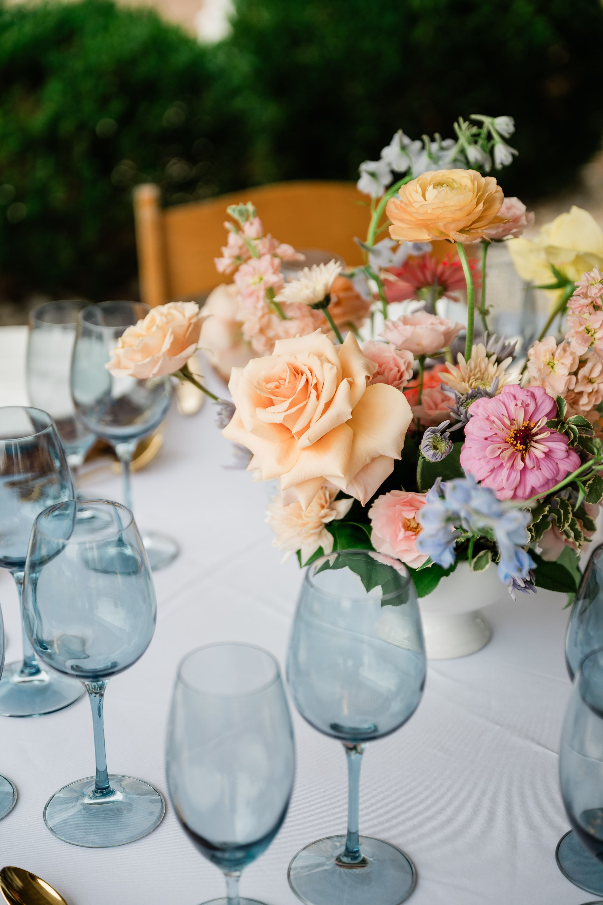 Elegant table setting with blue wine glasses and peach rose centerpiece on white tablecloth.
