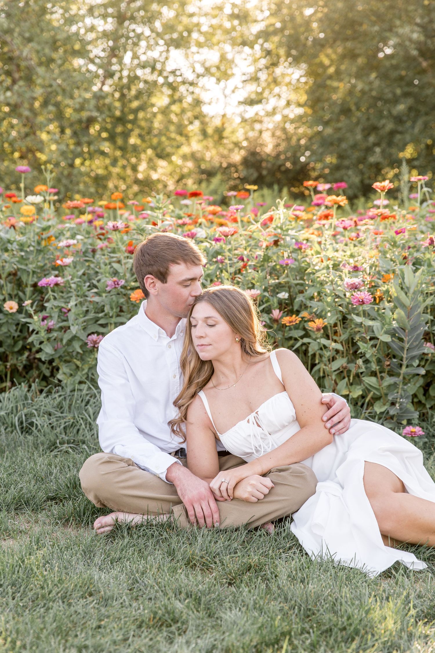 Romantic outdoor portrait of couple sitting together in blooming garden at sunset with vibrant orange and red flowers.