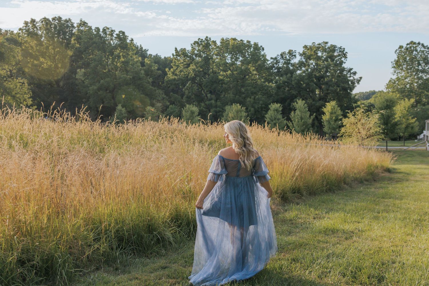 Woman in flowing dress walks through golden summer field at sunset.
