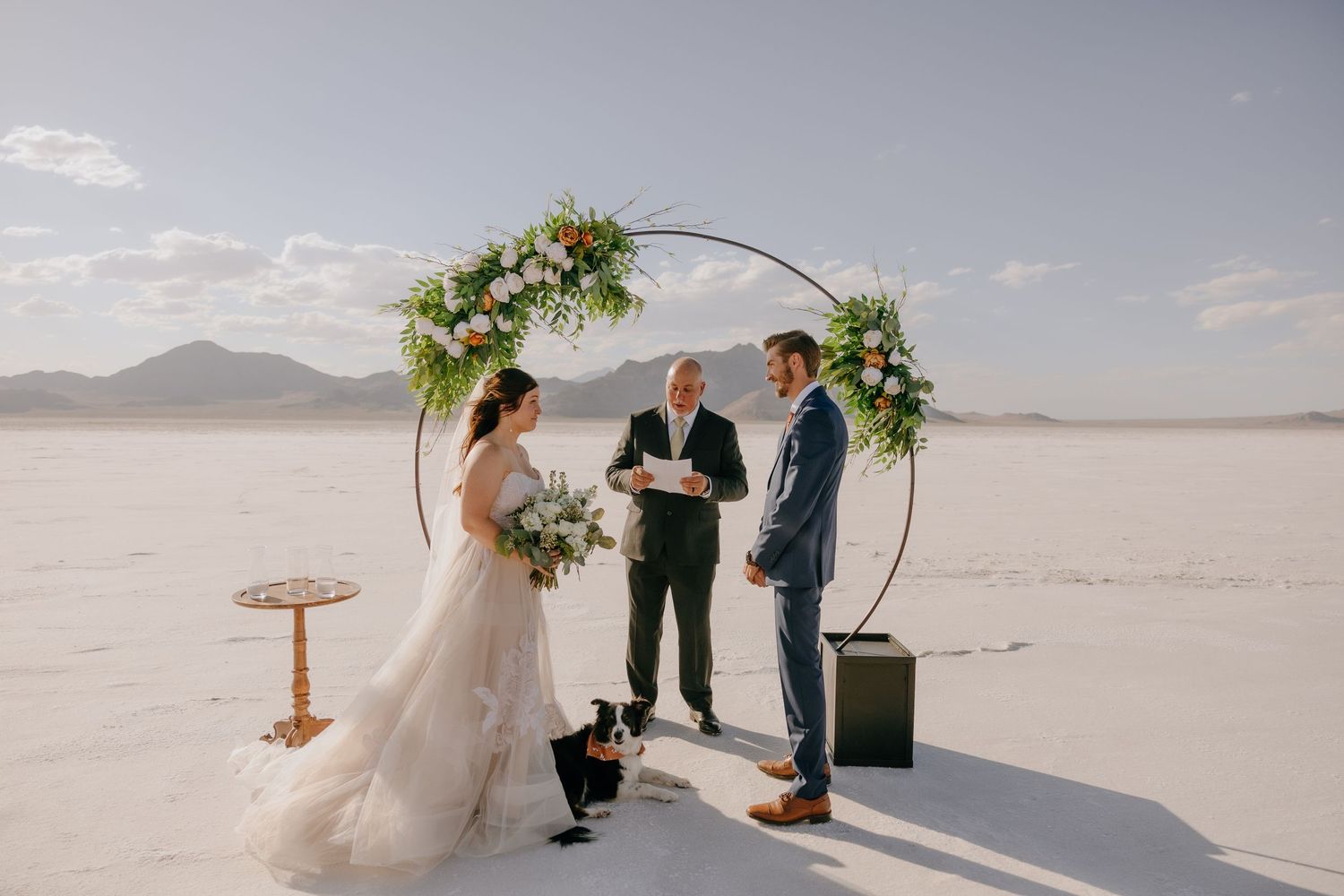 Bride and groom exchanging vows under a circular floral arch on the Bonneville Salt Flats.