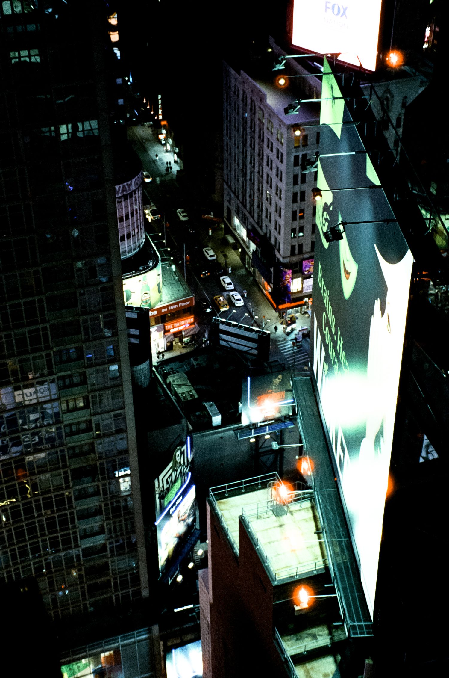 Aerial nighttime view of illuminated city buildings and billboards in an urban landscape.