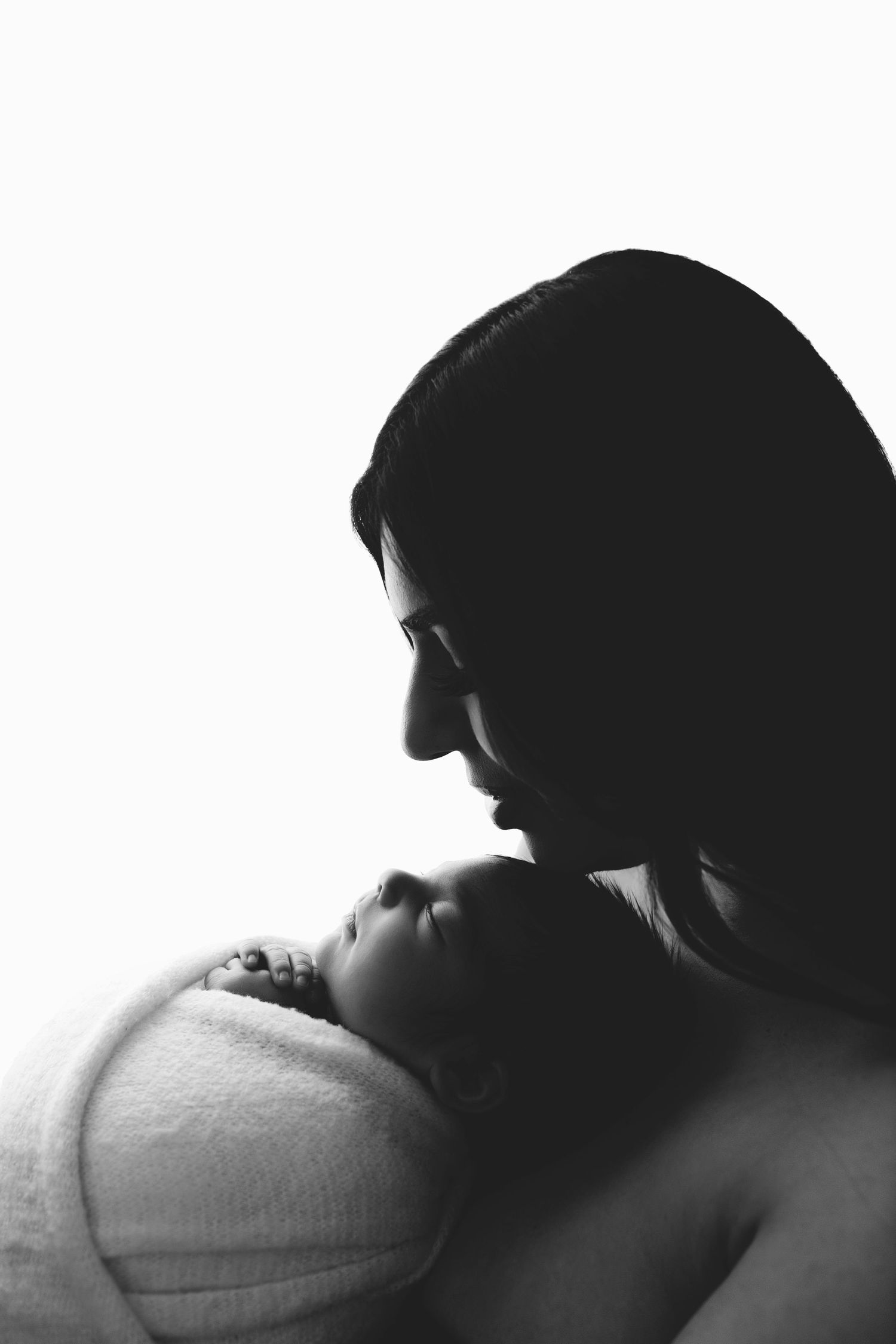 Sweet sleepy newborn snuggled with soft white teddy bear on white blanket in studio setting.