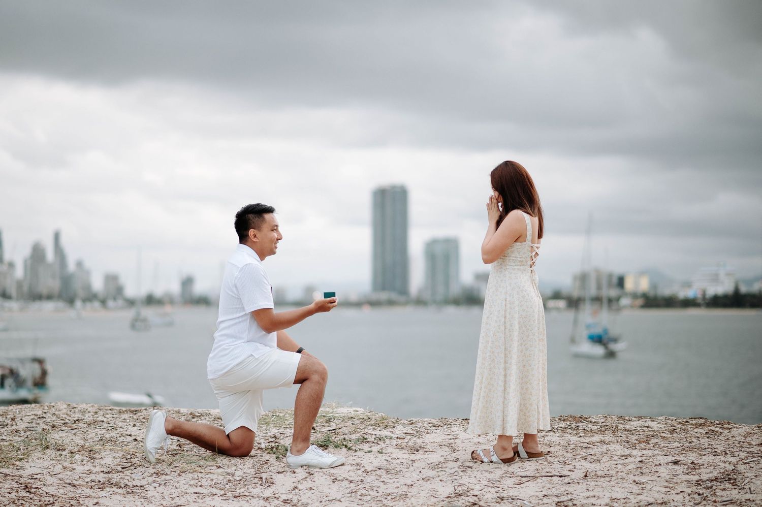 A romantic beach proposal scene with harbor and city skyline as backdrop.