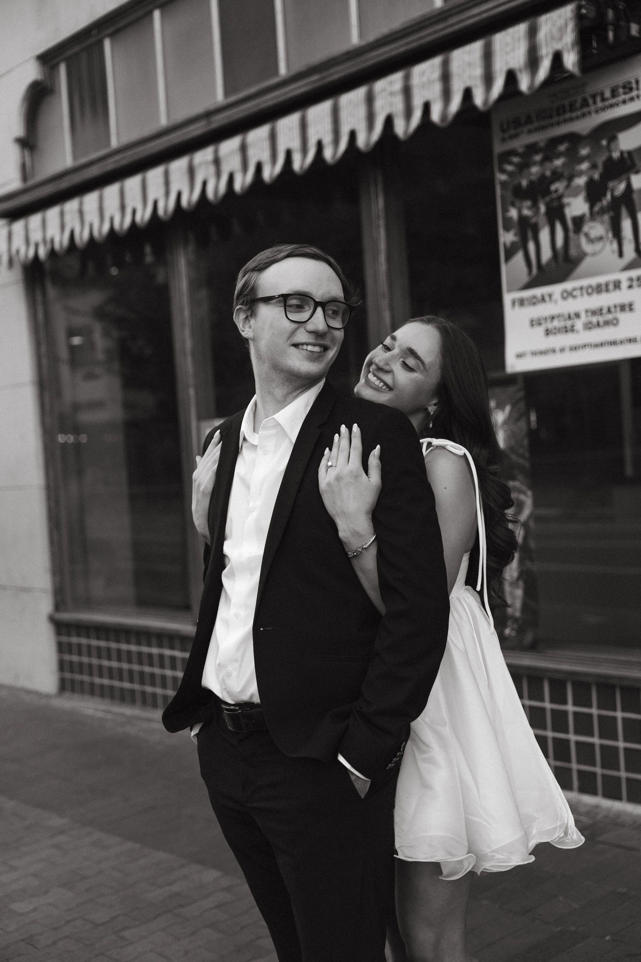 A romantic black and white portrait in front of a vintage storefront with an awning.