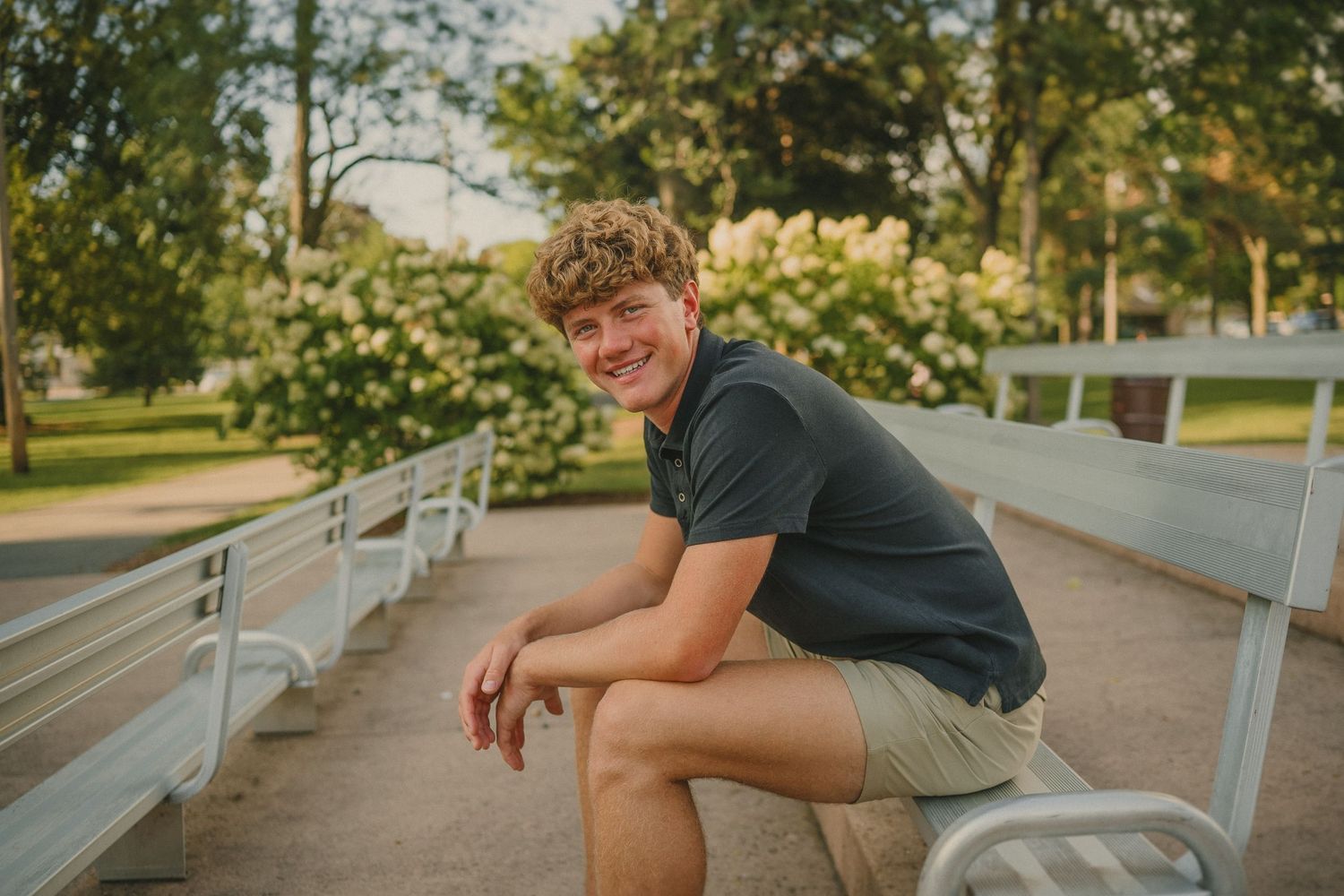 Person in a dark shirt and khaki shorts sitting casually on bleachers at a park during golden hour.