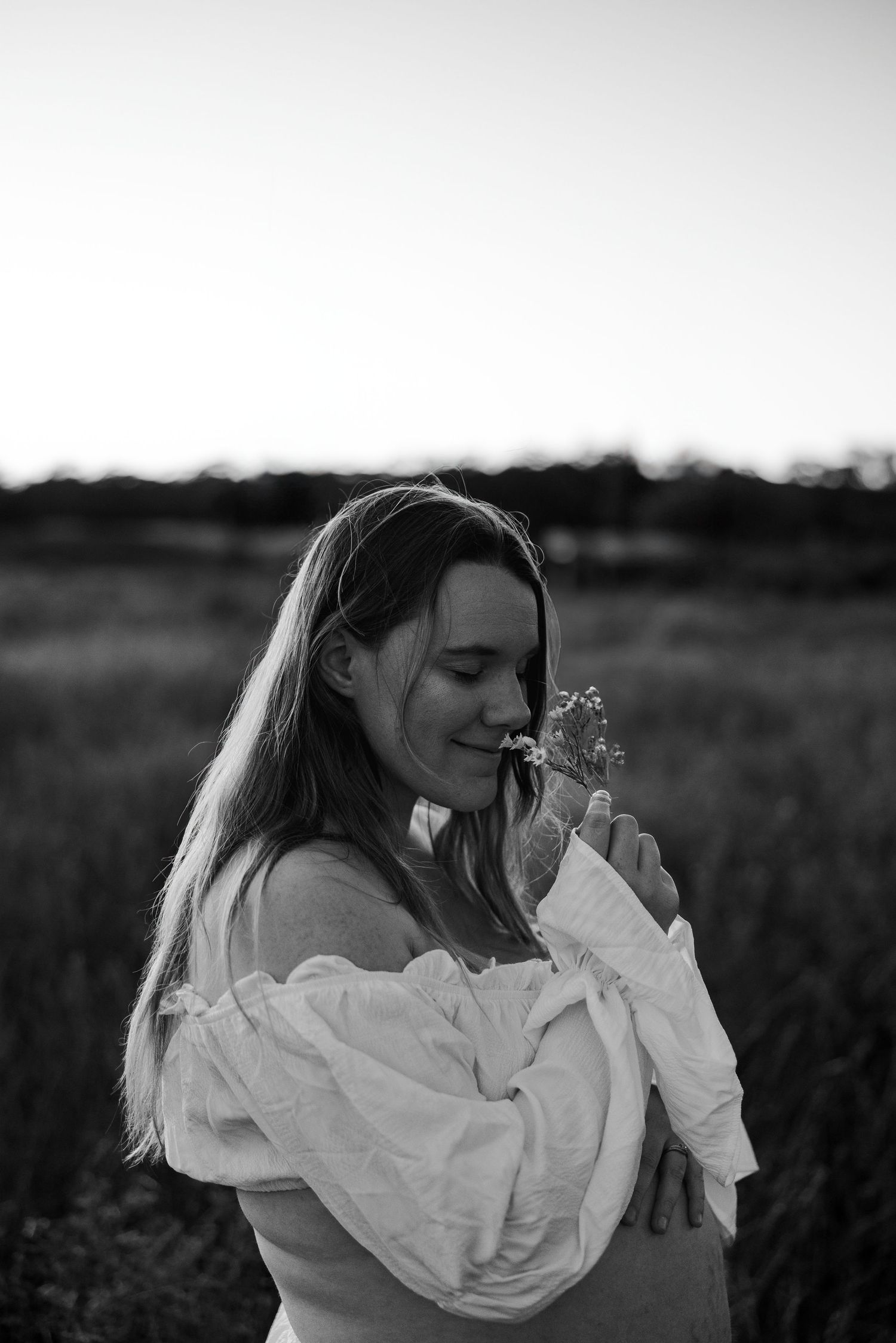 A person in a flowing white dress walks through a sunlit field with a small child at sunset.