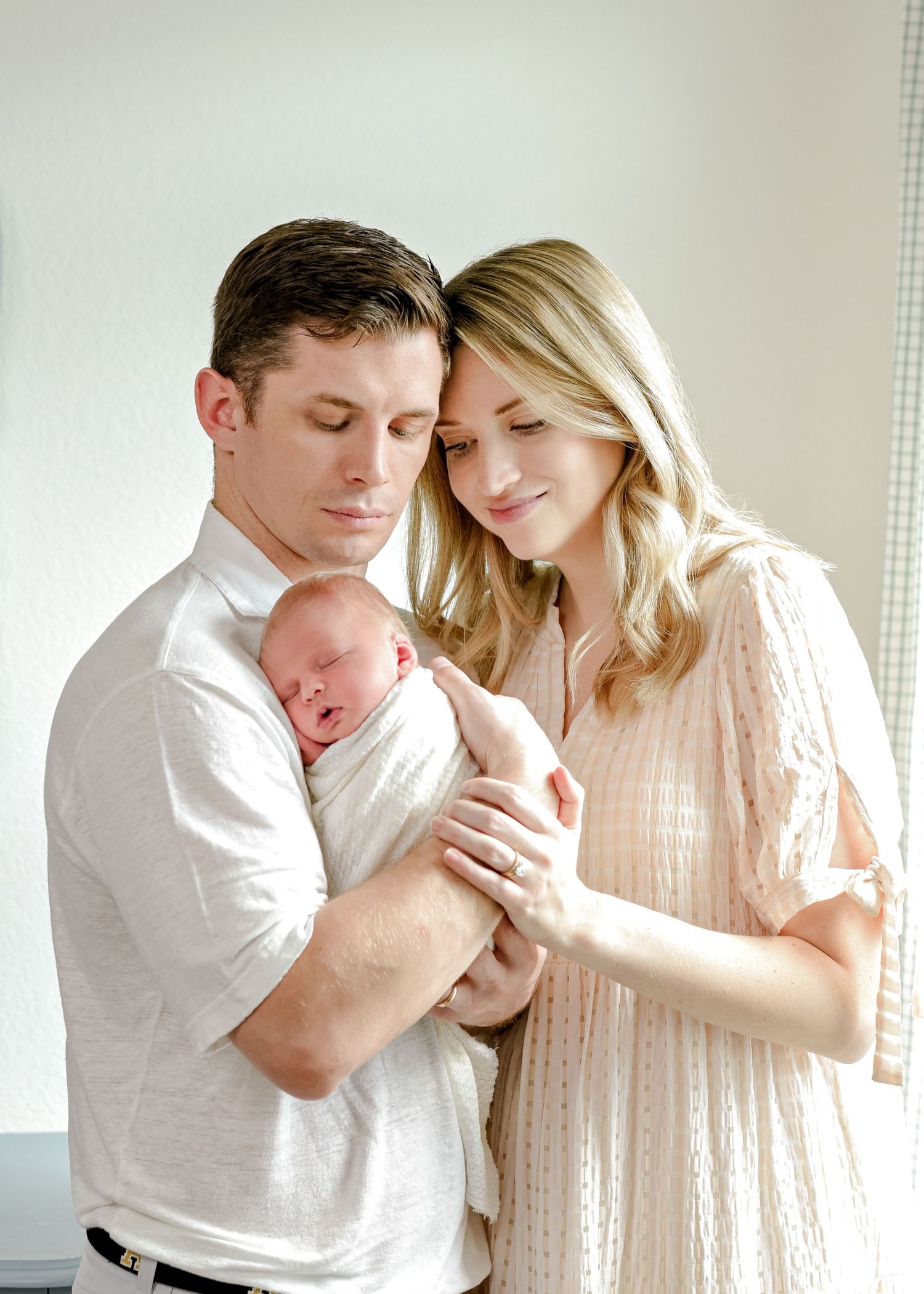 Intimate family portrait with newborn baby in white setting.