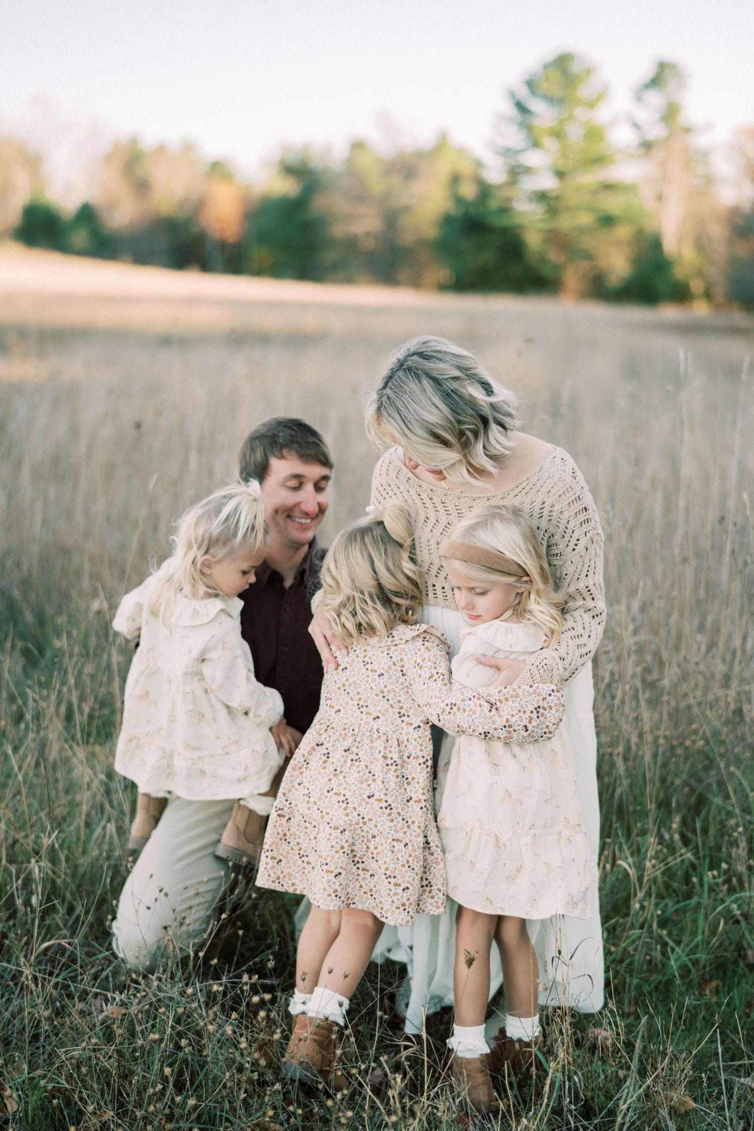 Family sharing tender moment together in tall grass field at golden hour.