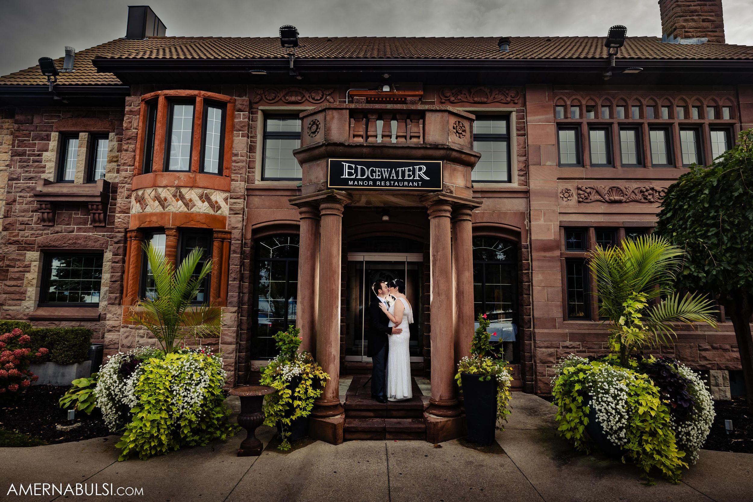 A couple stands in front of a brick Brunswick restaurant entrance adorned with lush greenery and potted palms.