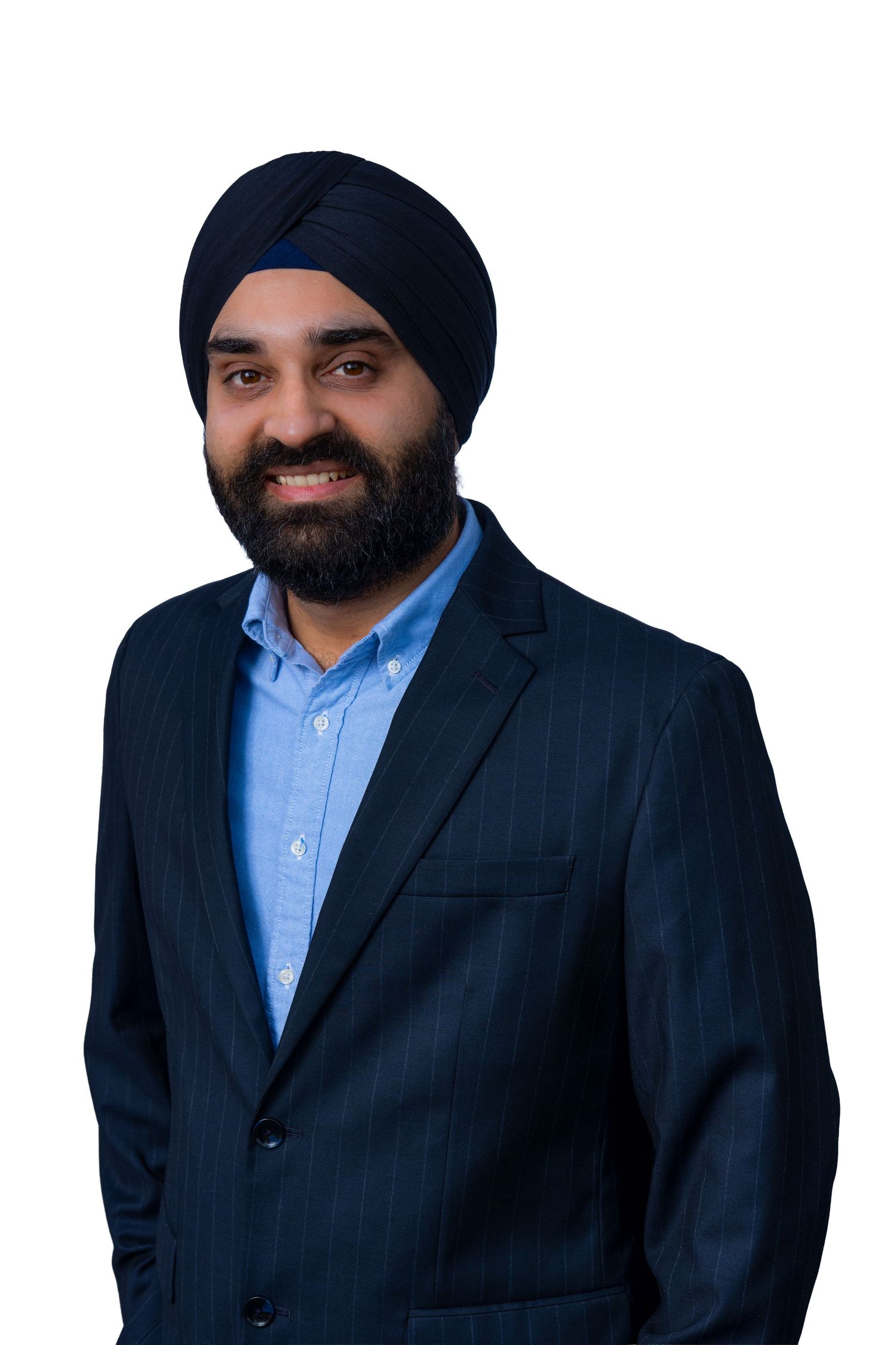 Professional business portrait of person wearing navy suit jacket, light blue dress shirt and dark turban against neutral background.