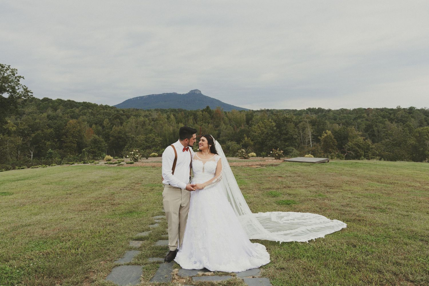 Wedding party in warm earth tones poses for panoramic photos together in a scenic grassy meadow landscape.