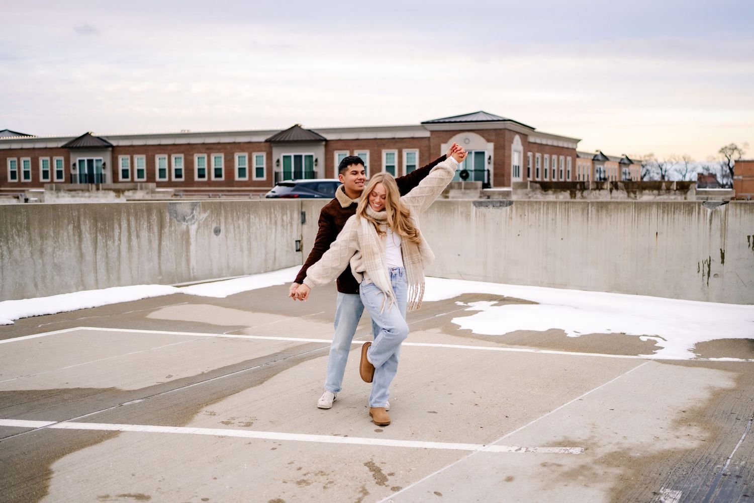 A person jumps playfully on a pier against a brick building backdrop on an overcast day.