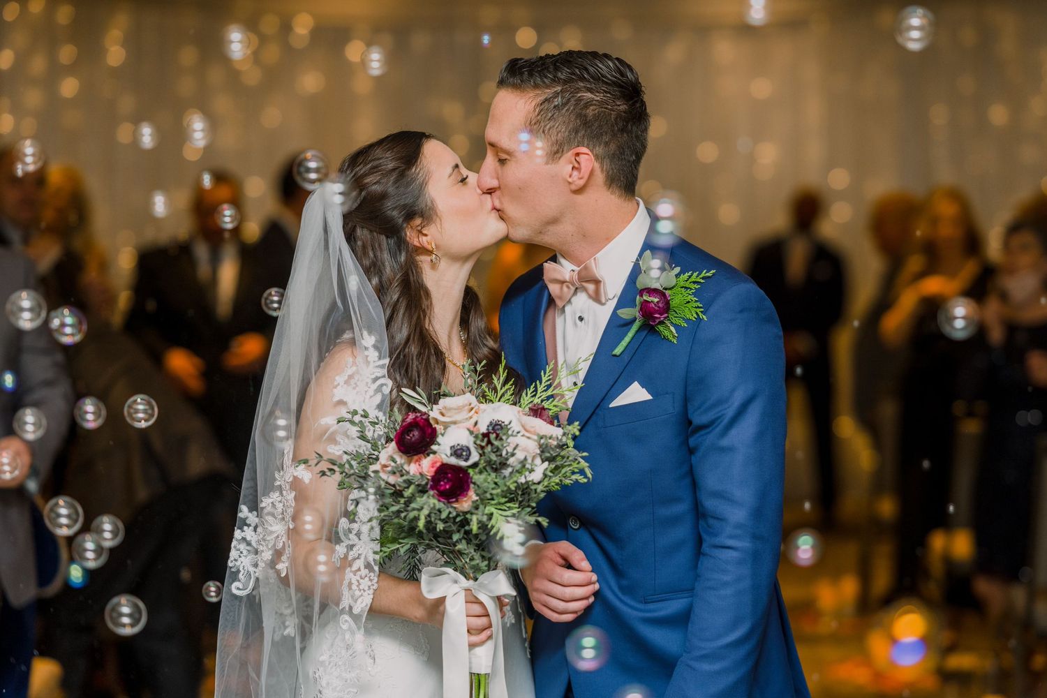 A wedding moment captured with bubbles floating in a golden-lit reception venue.