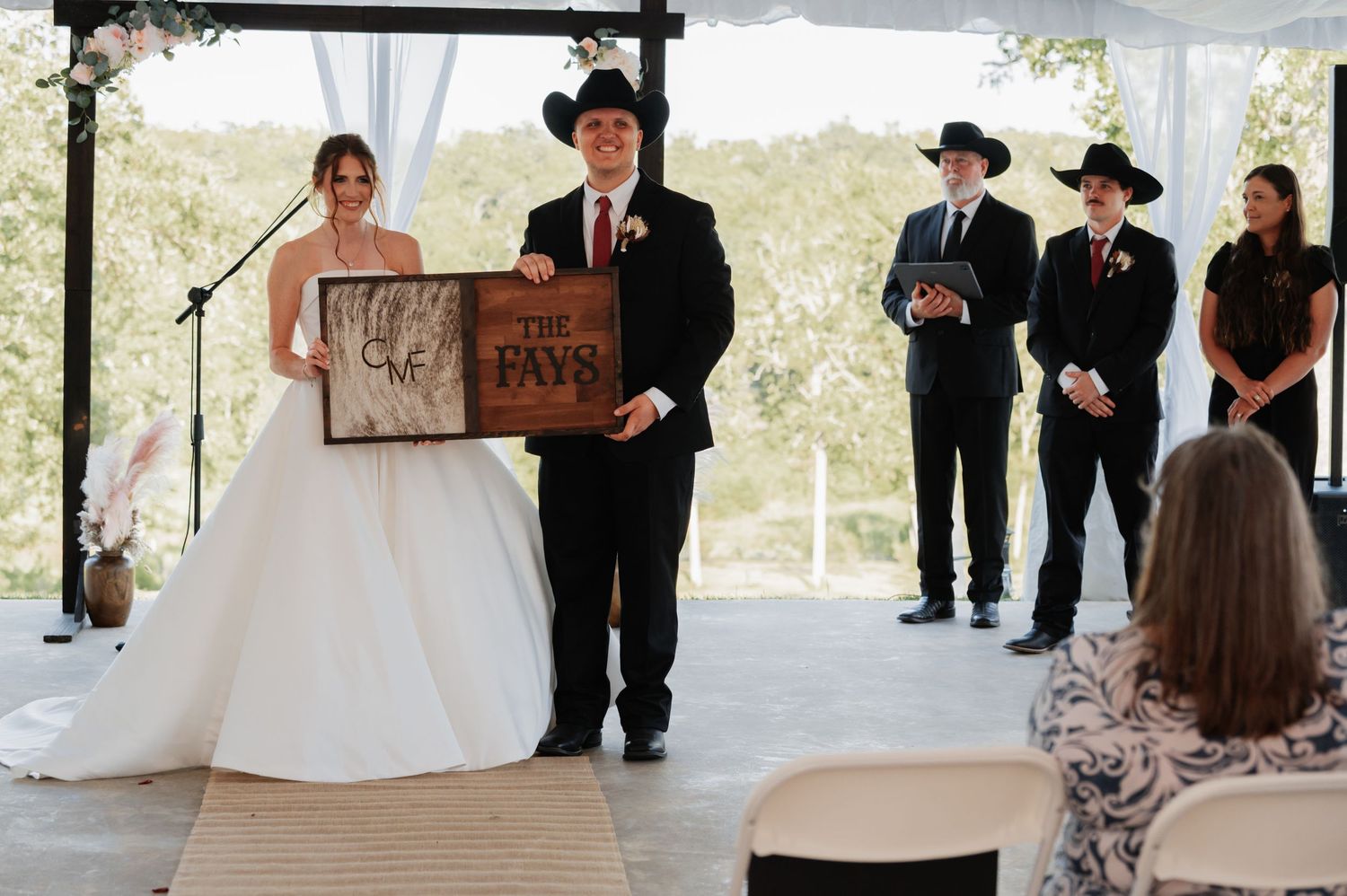 Bride and groom exchange vows at rustic indoor wedding ceremony with white chairs and floral arrangements.