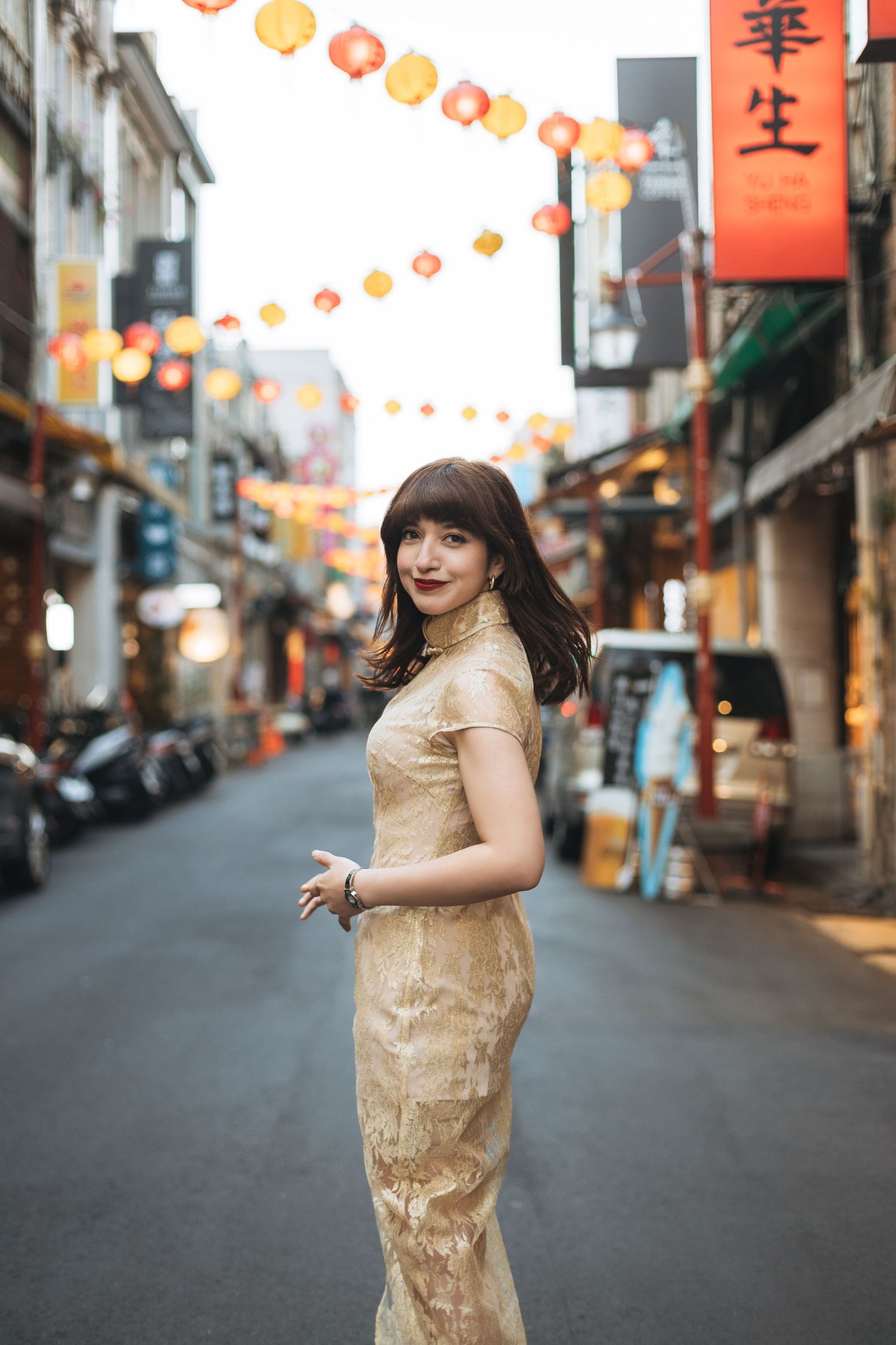 Woman in gold qipao dress posing on a street decorated with Chinese lanterns.