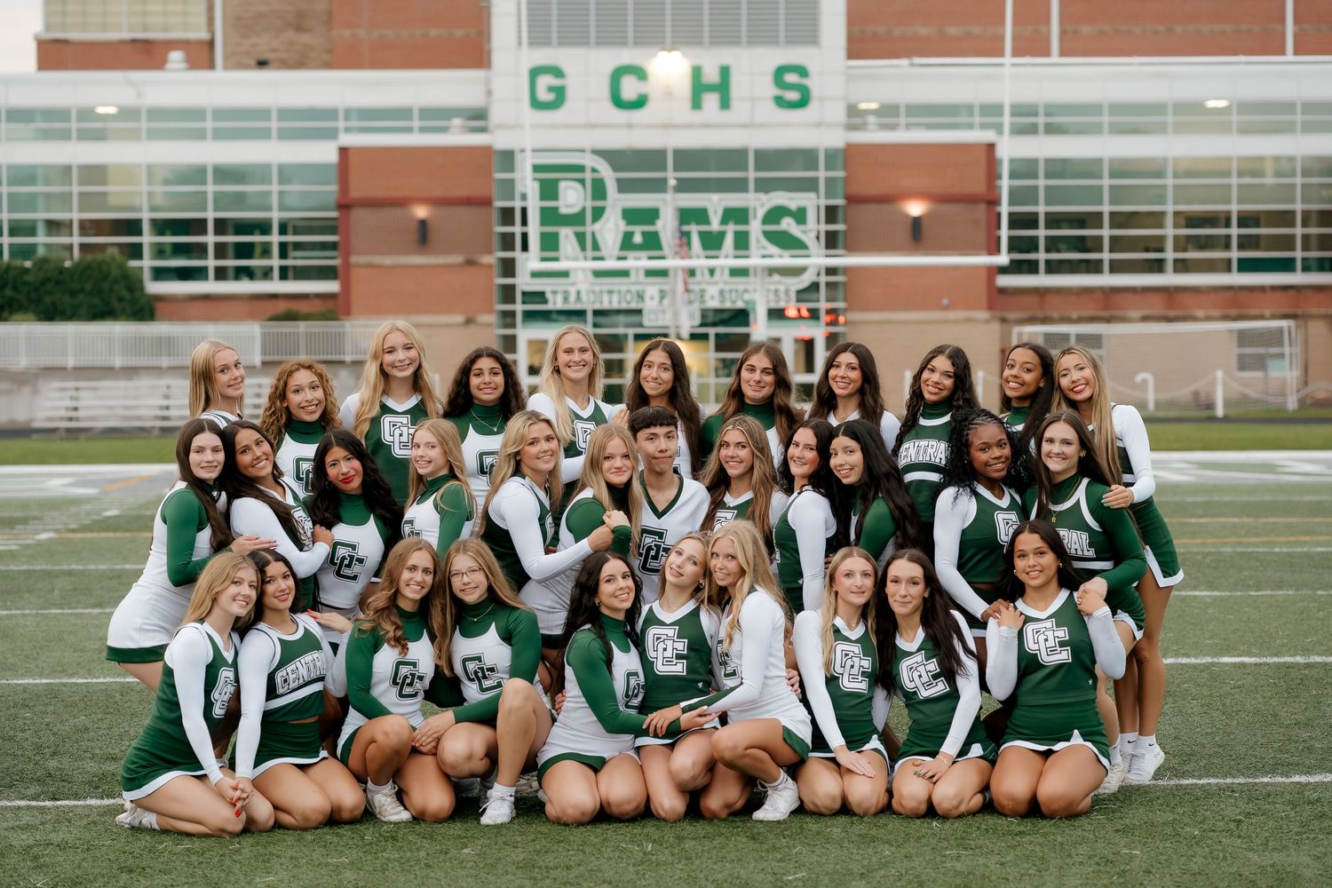 GCHS Rams cheerleading squad poses together on the football field in green and white uniforms for a team photo.