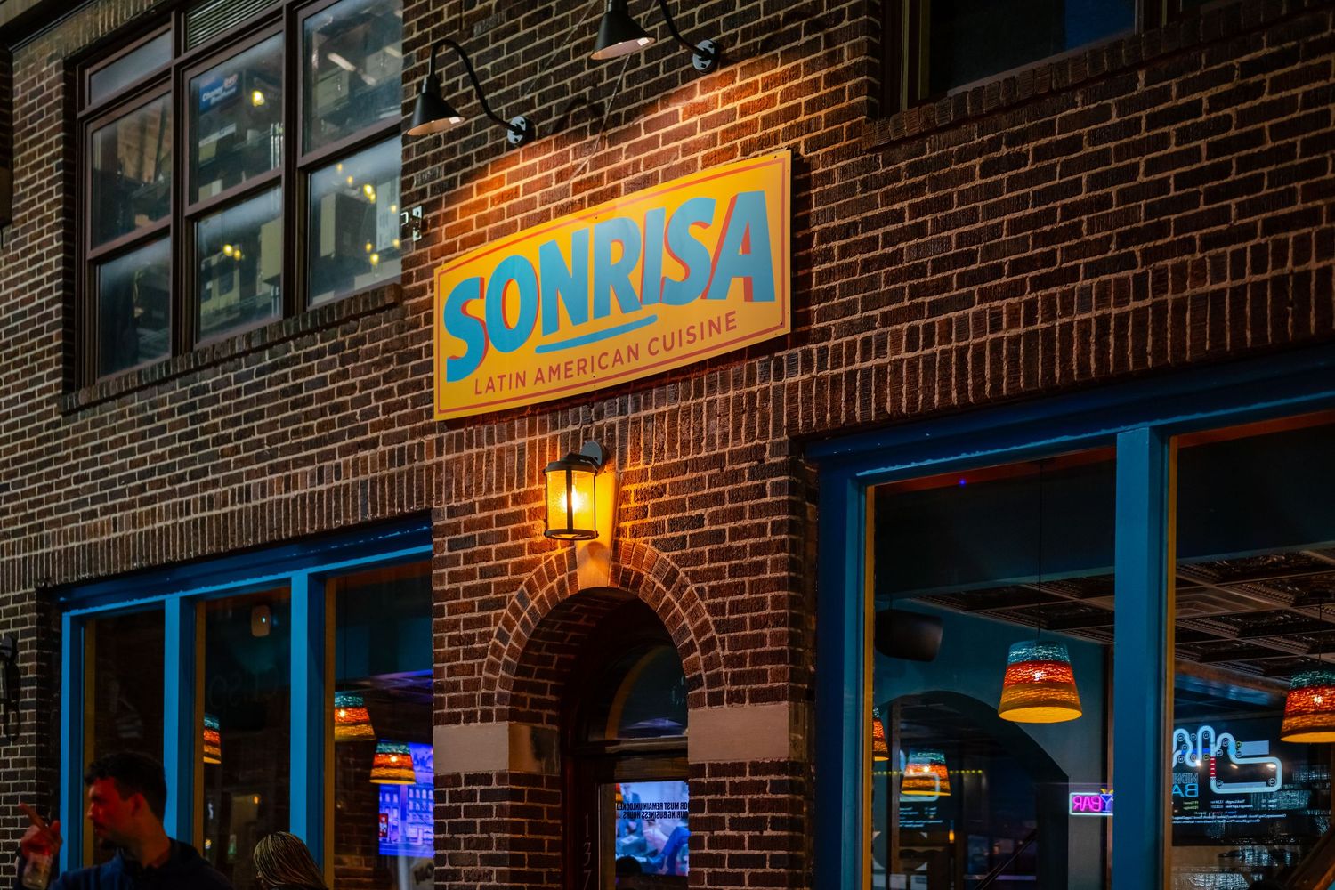 Sonrisa Latin American Cuisine restaurant exterior with glowing sign on brick building at night.