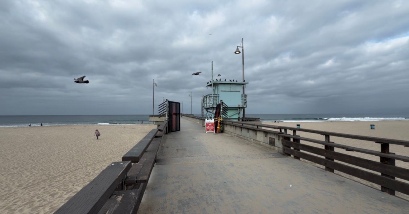 A cloudy day on a beach pier with a lifeguard tower, wooden railings, and sandy shore stretching into the distance.