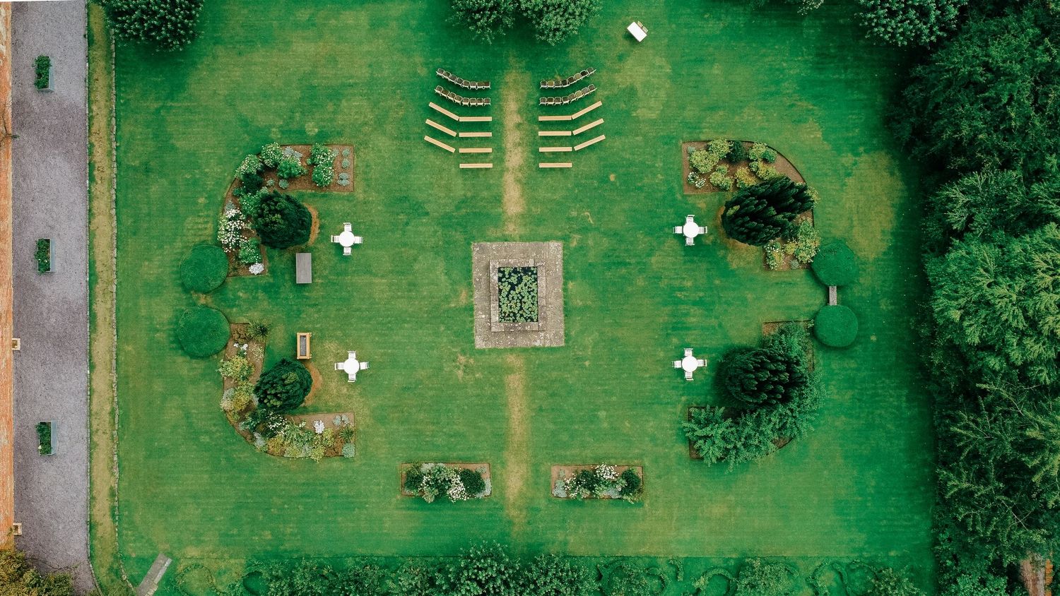 Aerial view of a symmetrical green garden with white cross markers, trimmed hedges, and a decorative central feature.