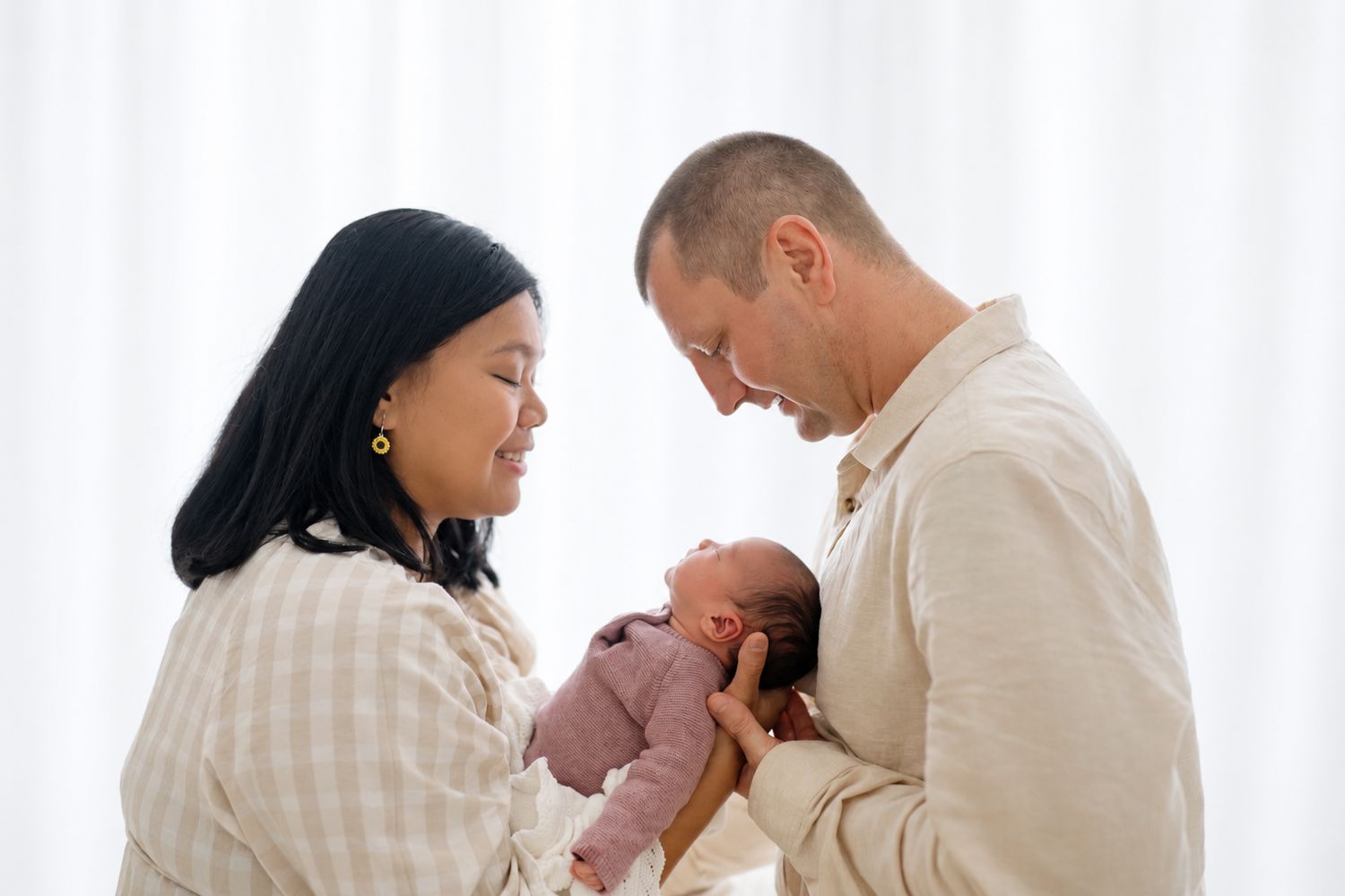 A couple lovingly gazes at their newborn baby, cradling the infant together in a bright, softly lit room.
