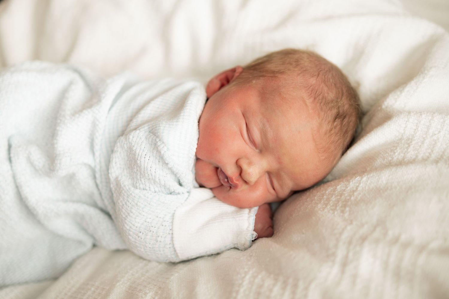 Peaceful newborn baby sleeping soundly wrapped in a soft white blanket, lying on white bedding at Parkwest Medical Center in Knoxville, TN.