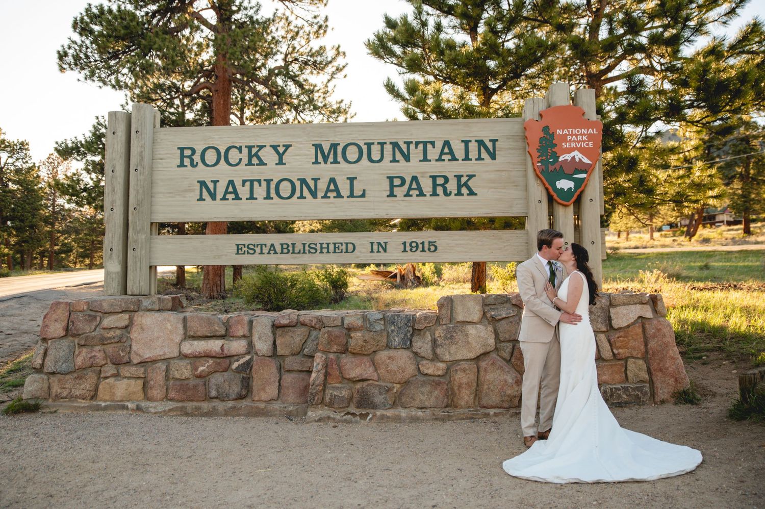 Wedding photo at the Rocky Mountain National Park entrance sign with mountain scenery.