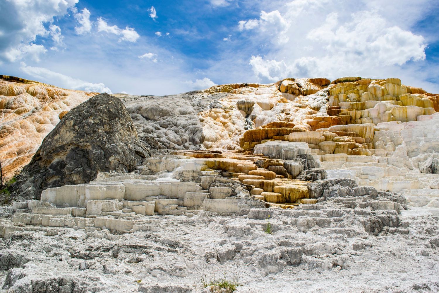 Mammoth Hot Springs terraces with steam rising under blue sky at Yellowstone National Park.