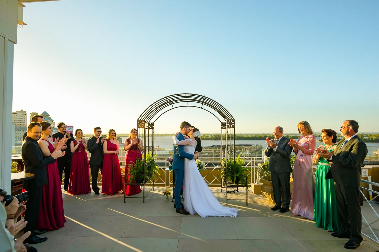 A wedding ceremony on a rooftop terrace with attendees in colorful formal attire gathered around an archway.