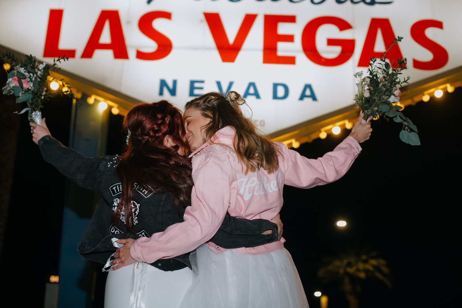 A couple celebrating under the iconic Las Vegas welcome sign at night.