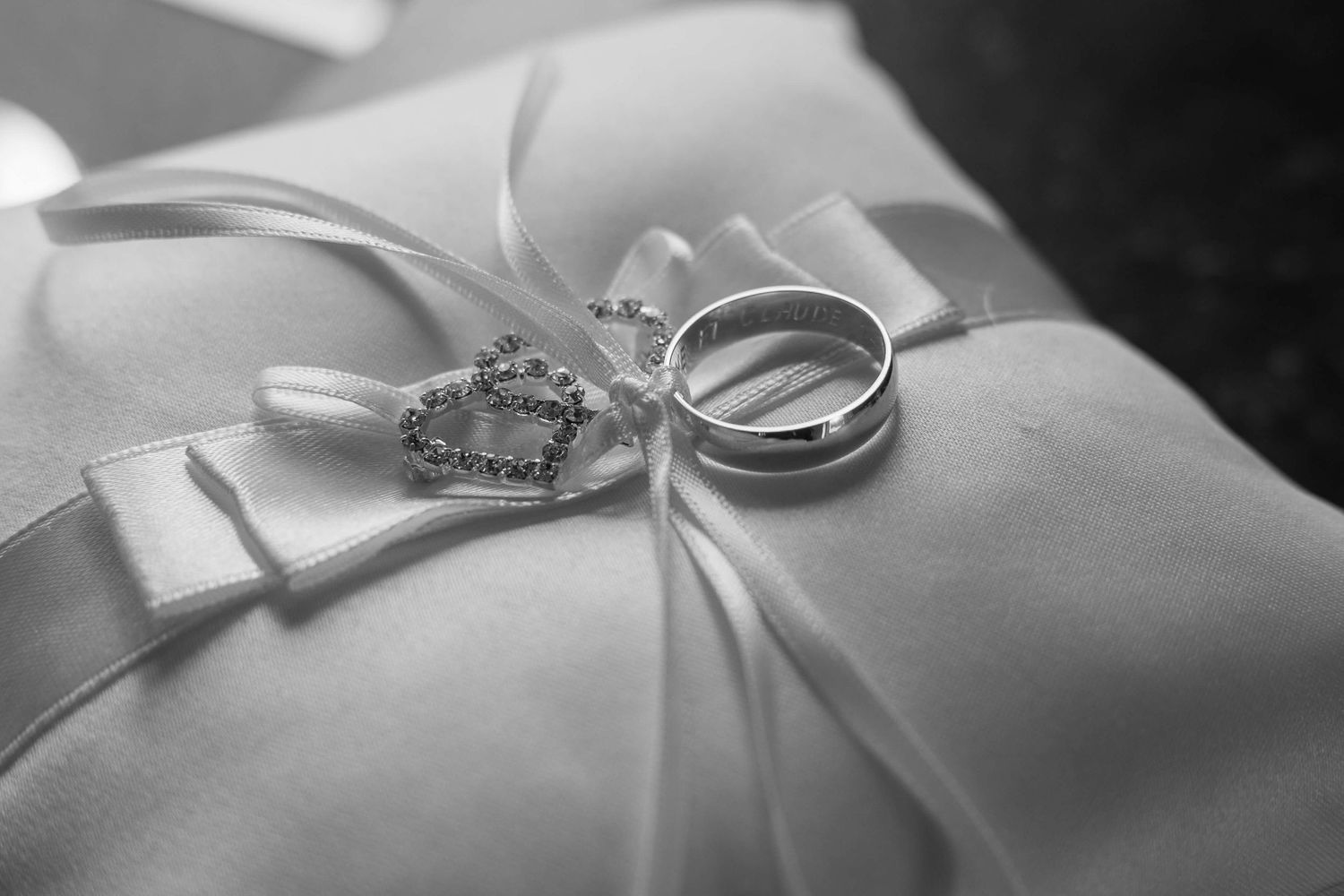 Wedding rings and ornate brooch displayed on white satin cushion with ribbon detail.