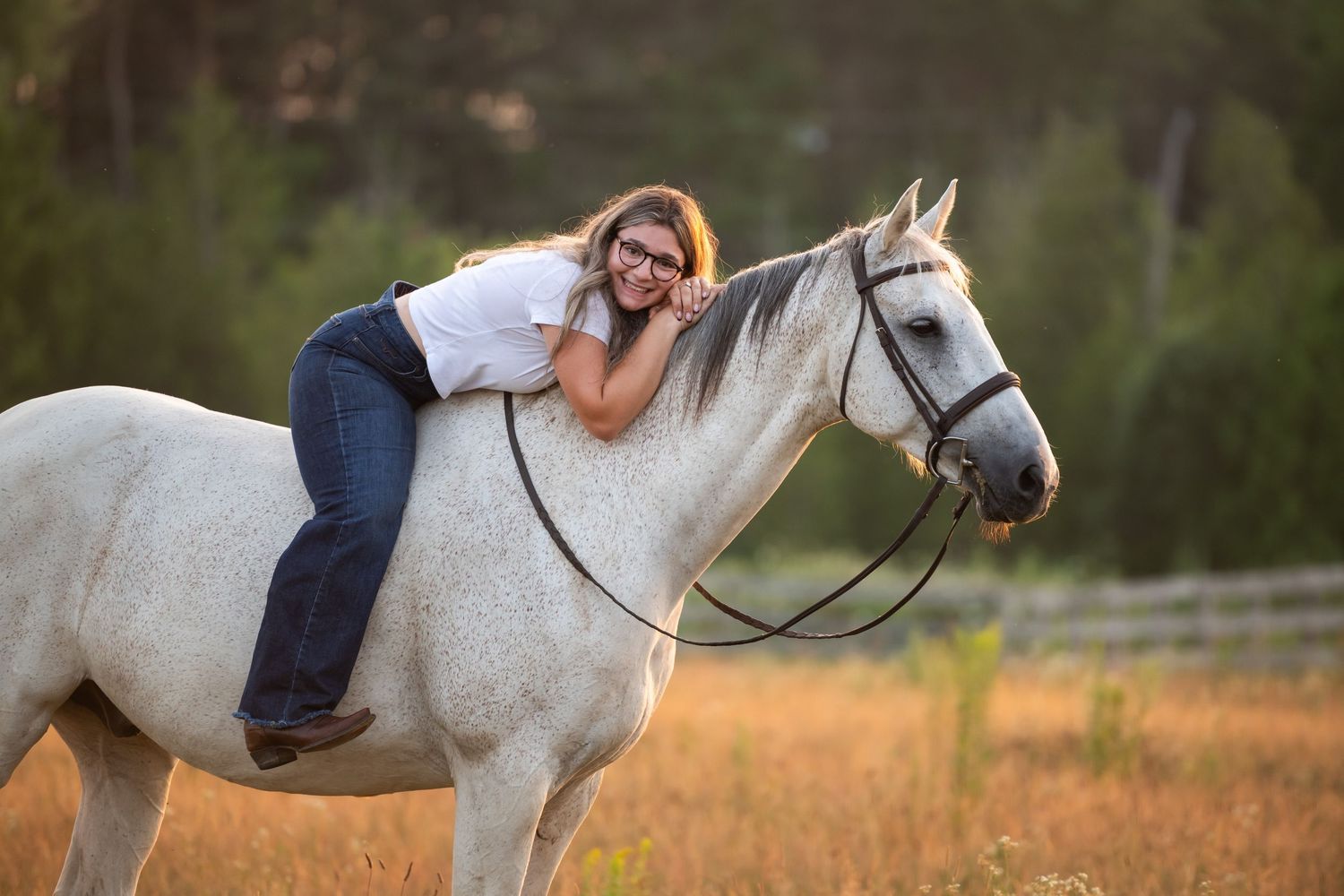 A woman in glasses leads a beautiful white horse along a peaceful rural dirt road on a sunny afternoon.