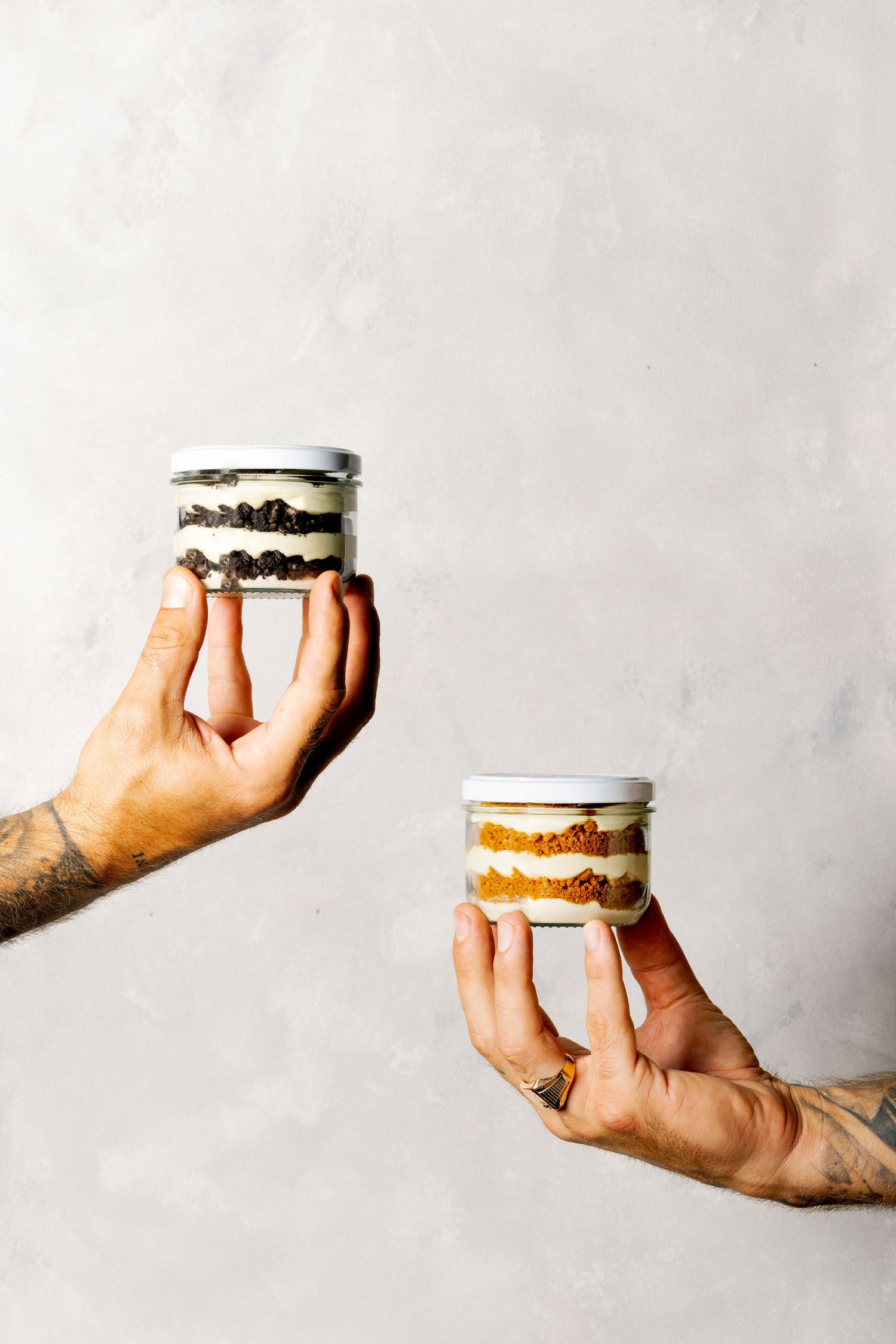 Hand holding a layered dessert in a small glass jar against a white background.