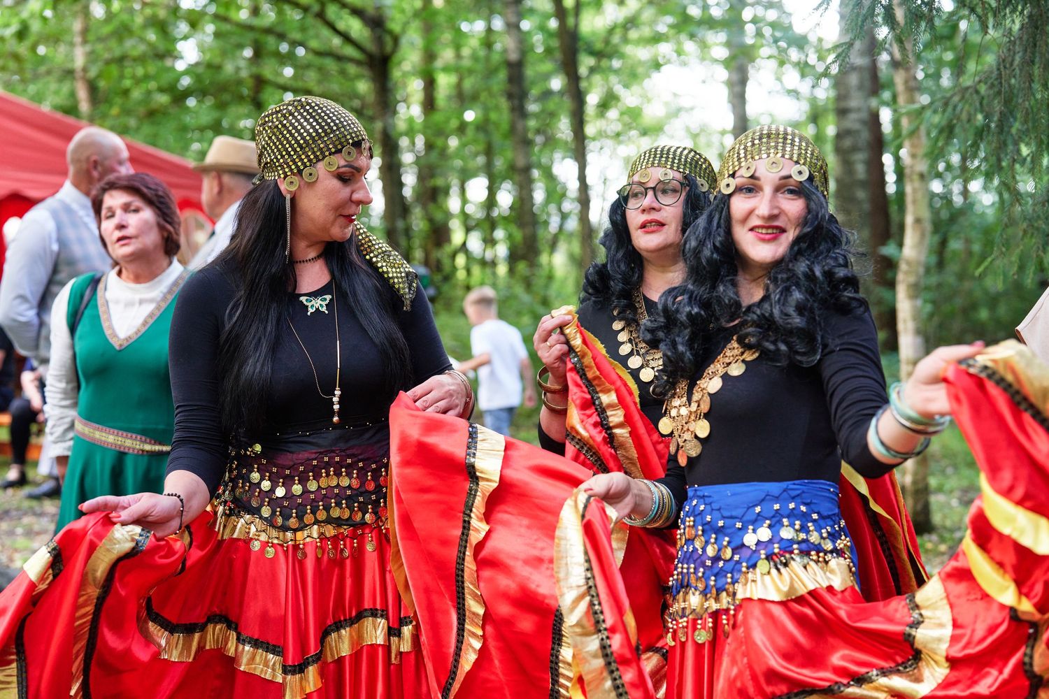 Group of women in traditional red dresses with decorative details dancing together outdoors.