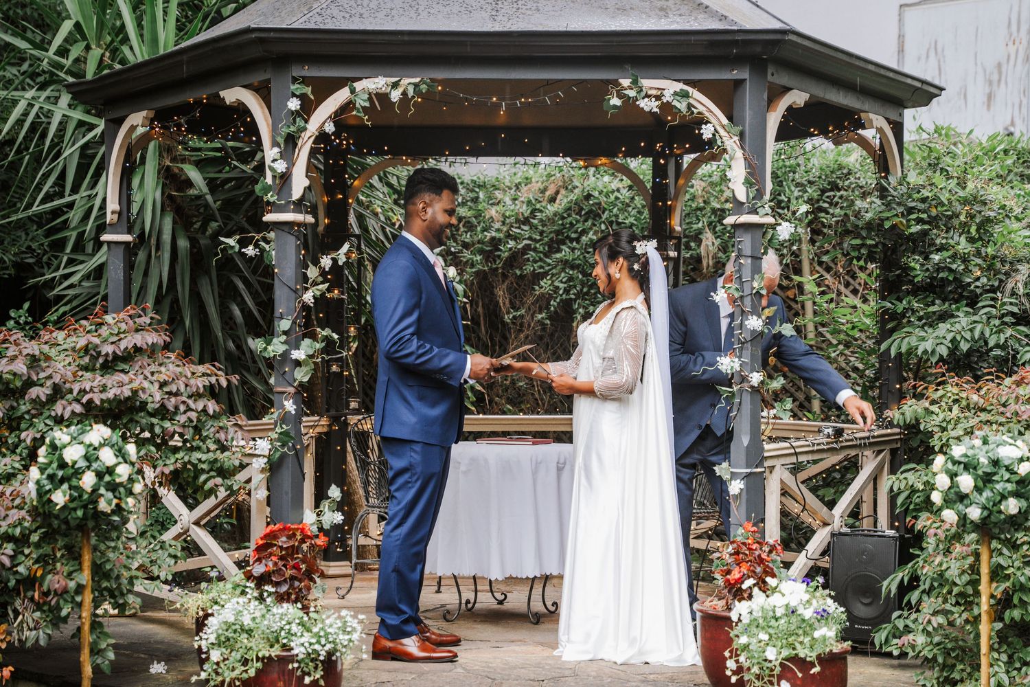 Elegant beach wedding ceremony under white arbor decorated with blush and white floral arrangements by the ocean.
