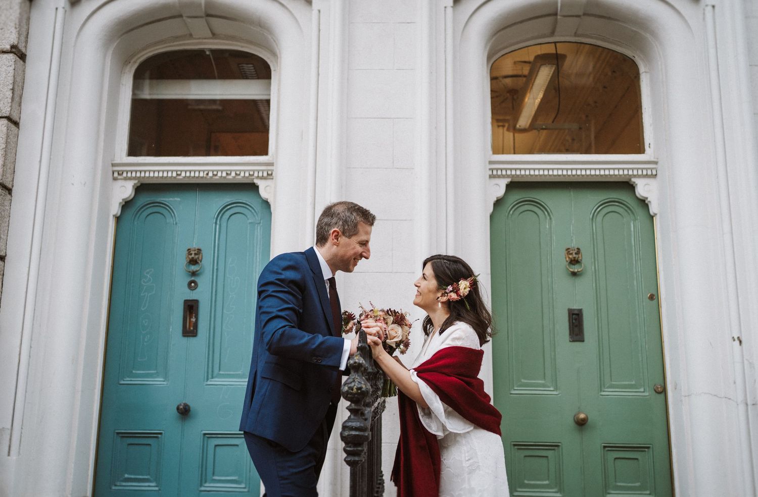 A couple in formal attire shares a romantic moment in front of a light blue door.