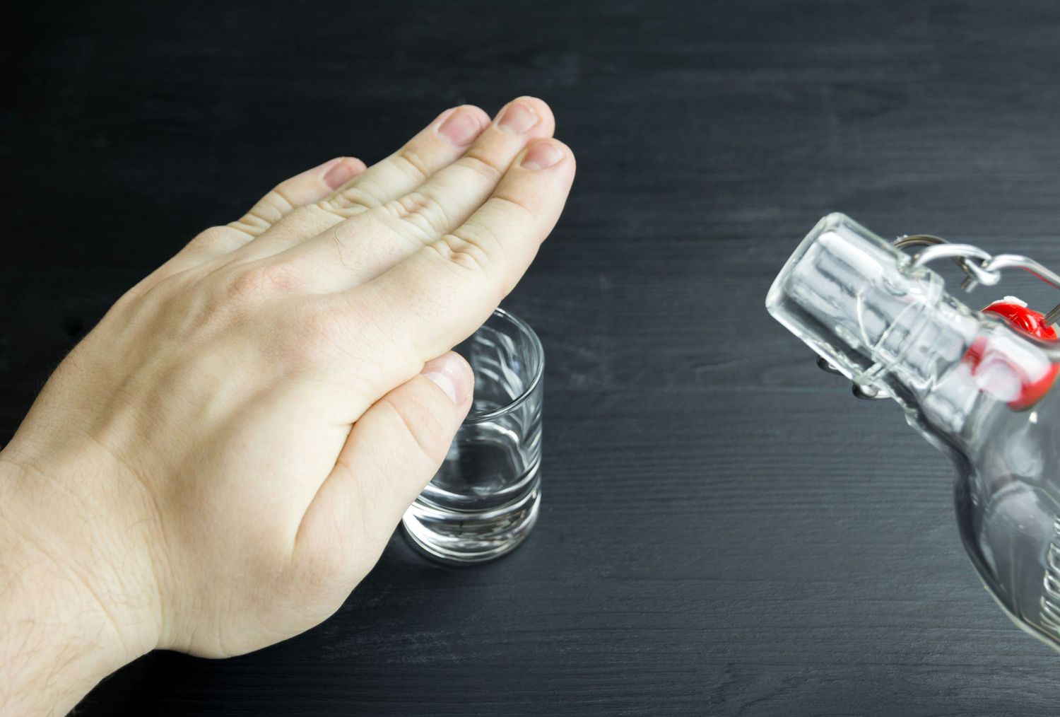 Hand pouring liquid from a glass bottle into a small container against a dark background.