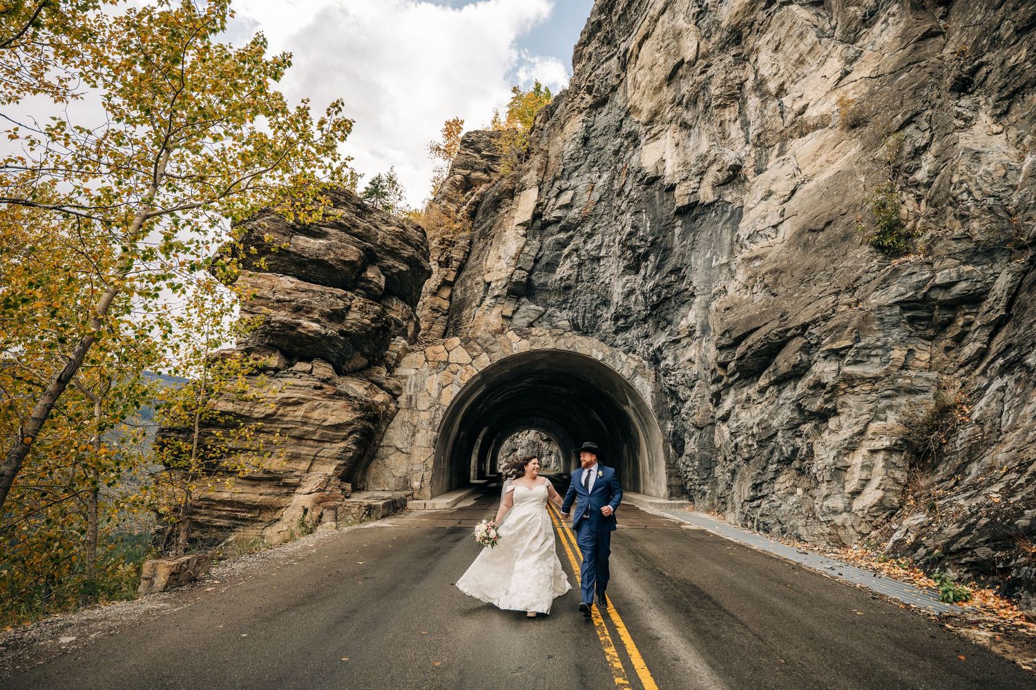 A wedding couple poses in a scenic mountain tunnel surrounded by autumn foliage and dramatic rock walls. Rising Sun Picnic Area Shoreline