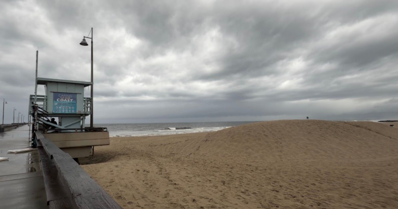 A panoramic view of a cloudy beach boardwalk with lifeguard stations and stormy skies over the ocean.
