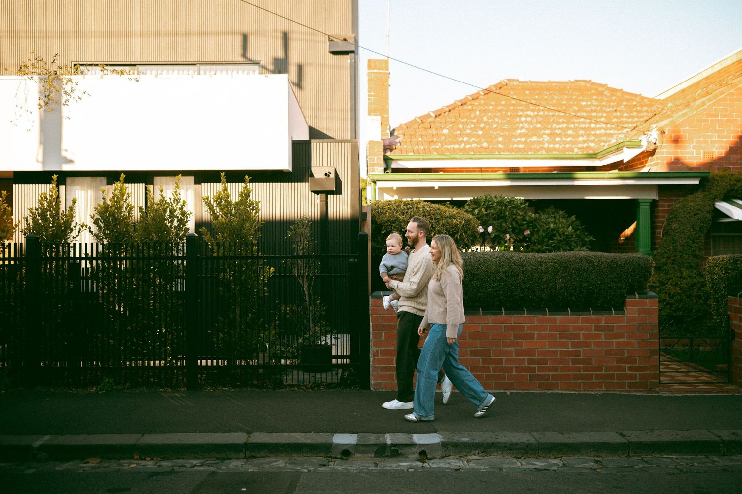 Young family walking together on a quiet Melbourne street during a relaxed neighbourhood photography session, with suburban homes.