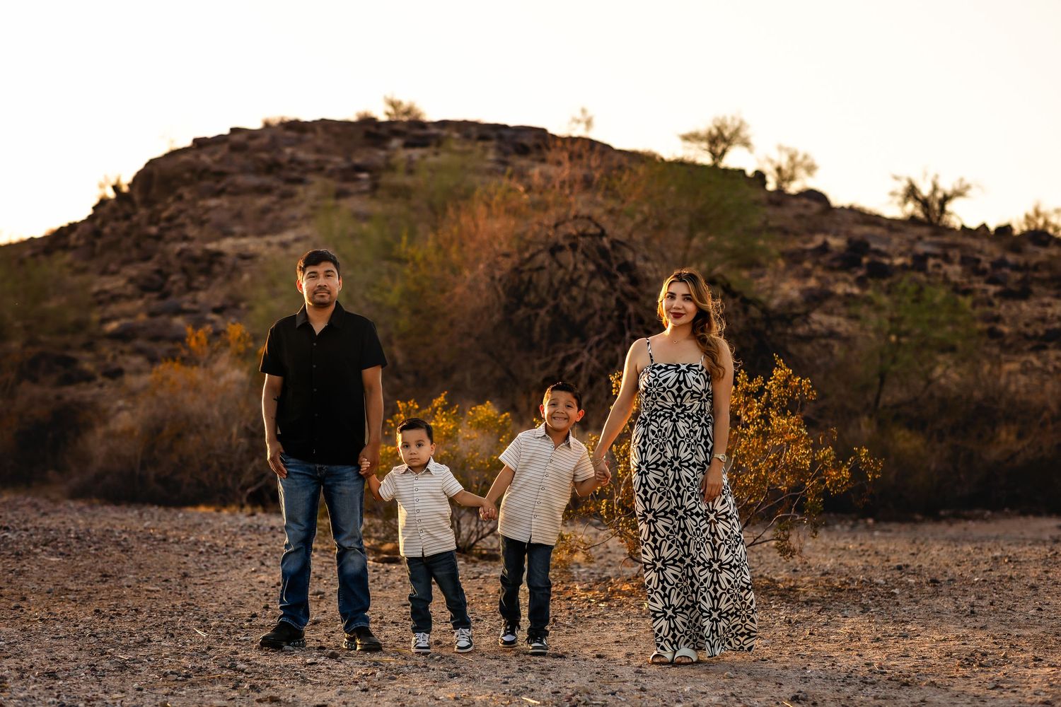Family poses together outdoors against a desert landscape during golden hour sunset.