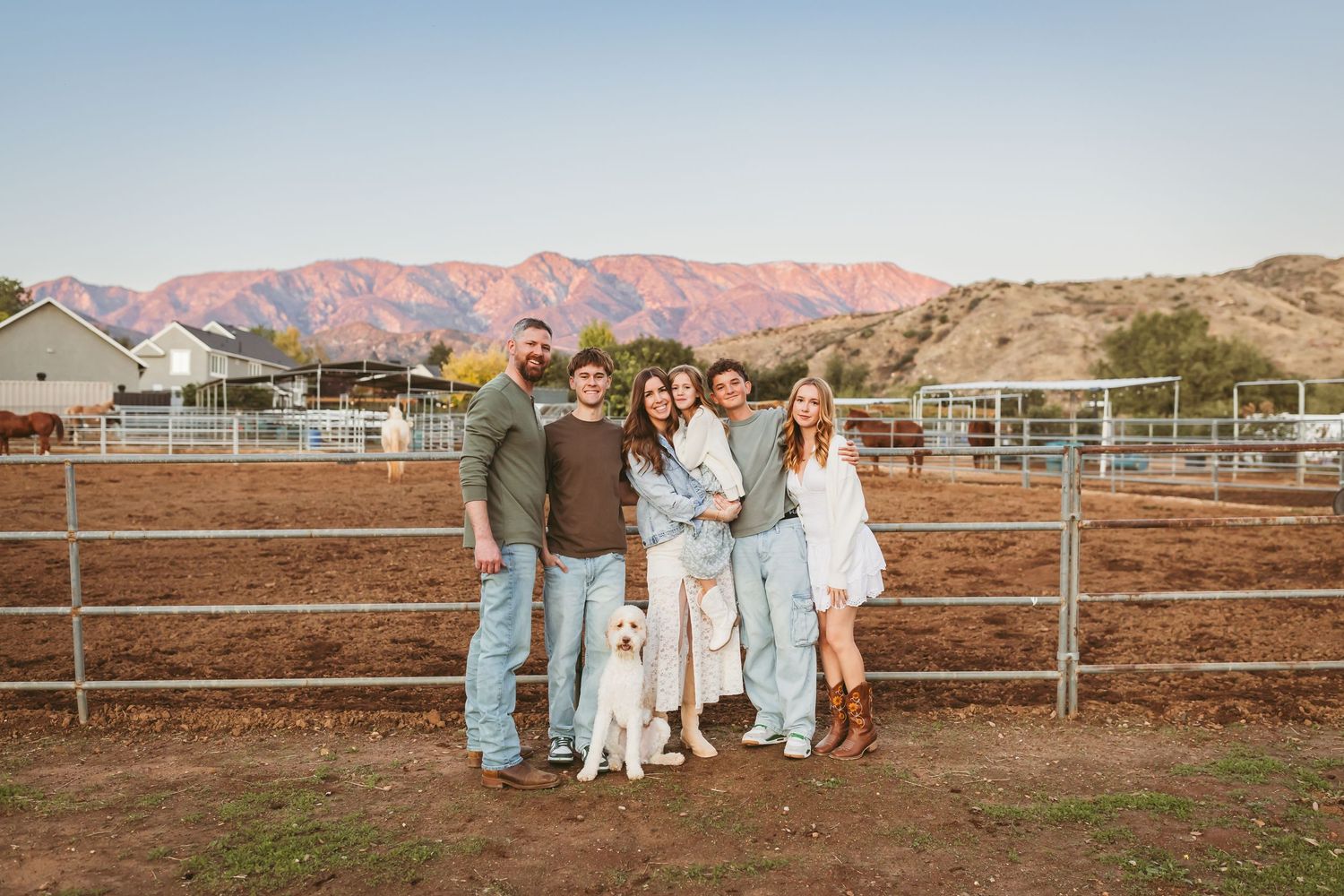 A group stands together at sunset by a metal fence with pink mountains in the background at a ranch.