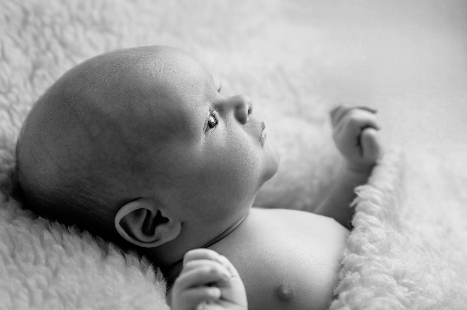 A sleeping baby rests peacefully on soft white fur bedding in a black and white photograph.