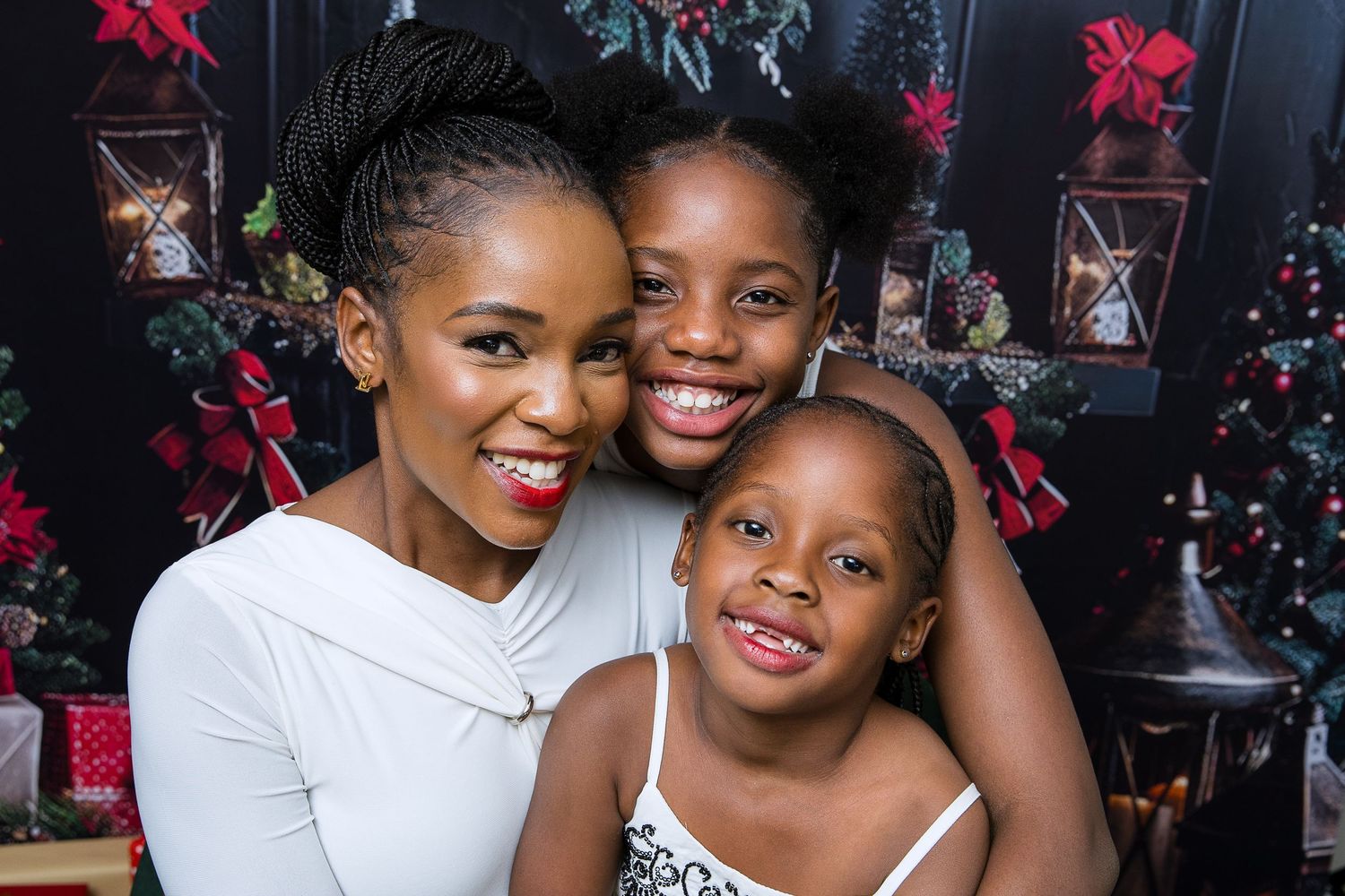 Three people smile warmly together in front of a festive holiday backdrop with red flowers and lanterns.