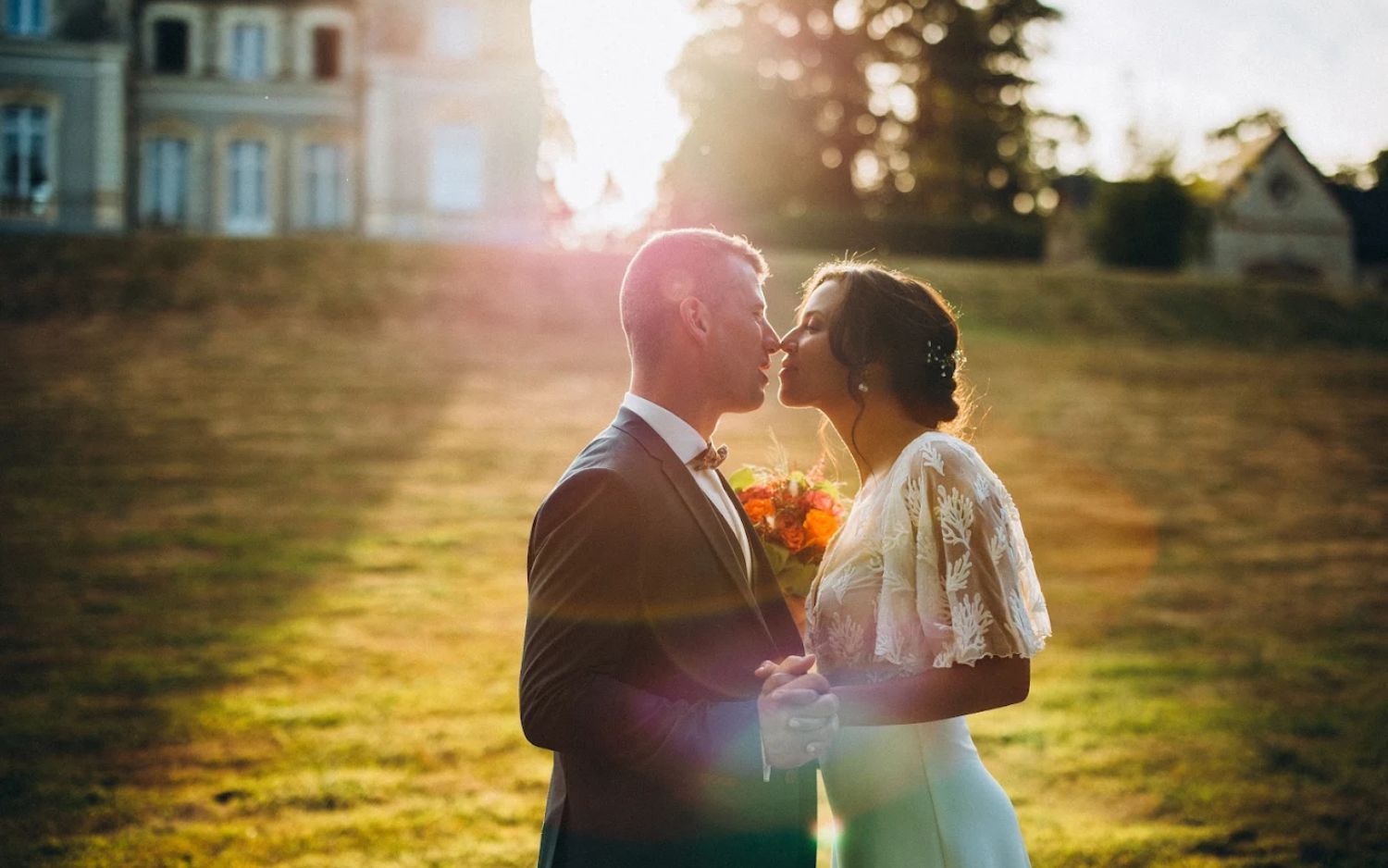 A romantic sunset wedding photo with a couple embracing on a grassy hill with golden sunlight streaming behind them.