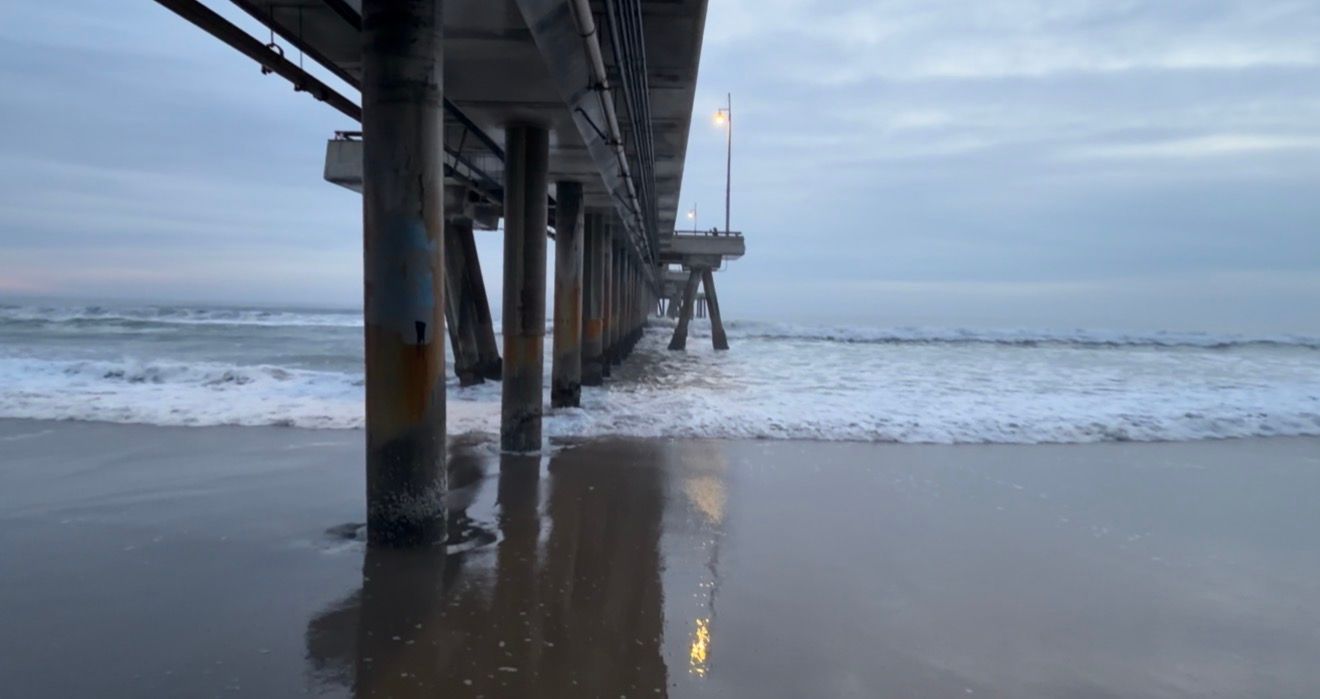 A series of connected photos showing waves crashing beneath a wooden pier at the beach during an overcast day.